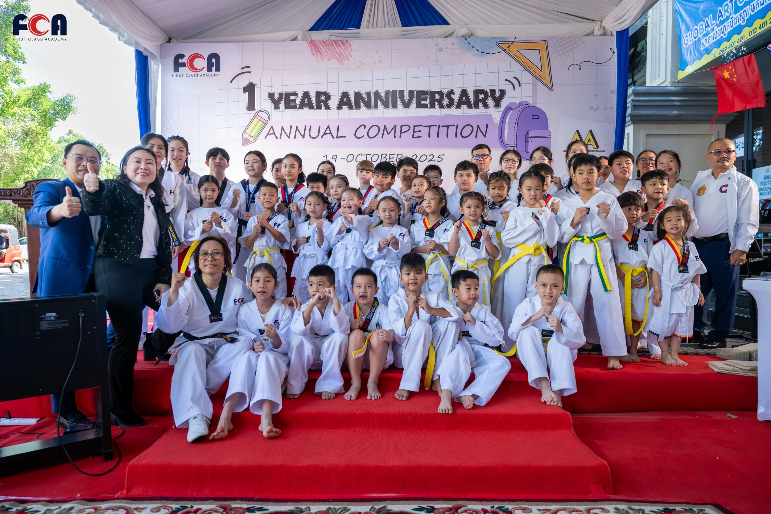 Group of children in martial arts uniforms on stage celebrating the first anniversary of FCA First Class Academy during their annual competition on October 19, 2025, with teachers and organizers.
