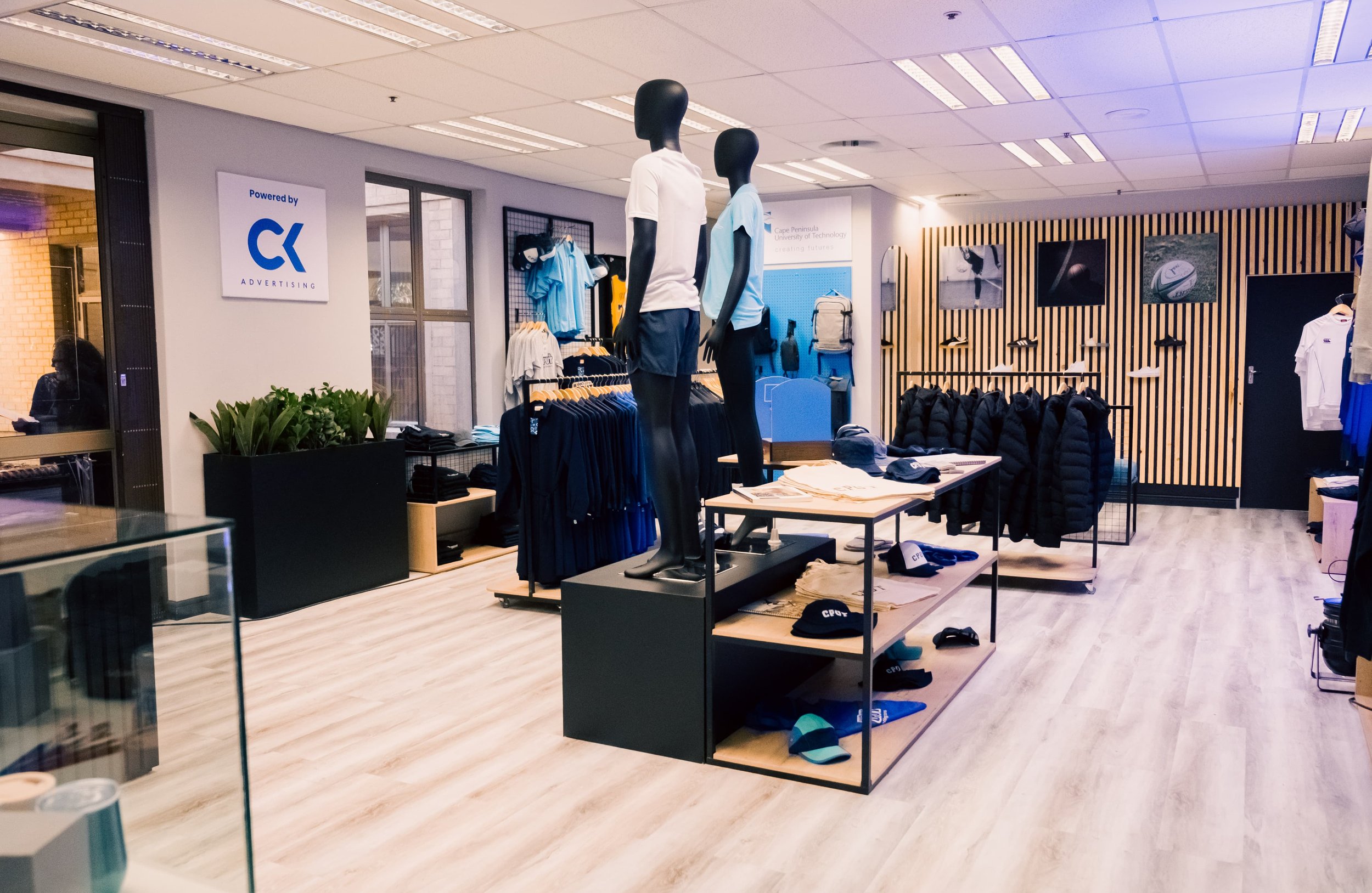 Inside a sports apparel store with mannequins dressed in athletic clothing, shelves of hats, and jackets displayed on racks and hooks.