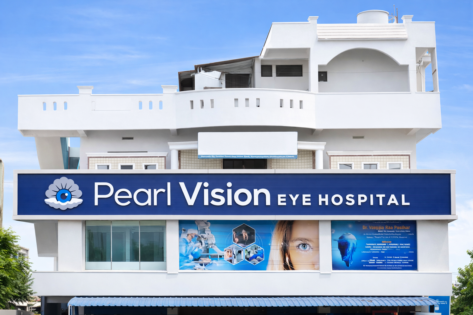 Front of Pearl Vision Eye Hospital with a blue sign featuring an eye logo, large windows, and promotional posters, with a white multi-story building in the background and a blue sky.