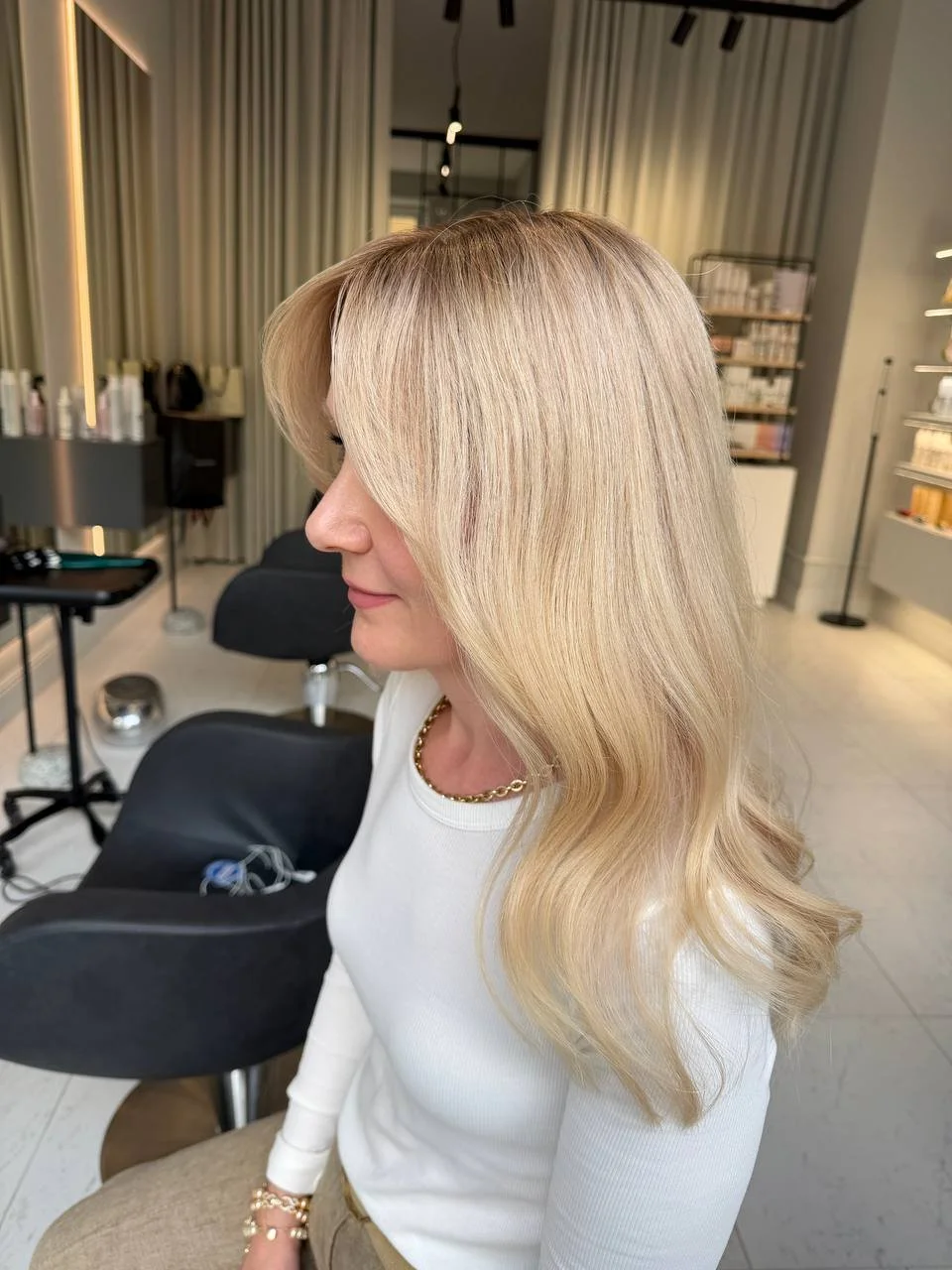 A woman with long, wavy blonde natural looking human hair wig sitting in a salon 