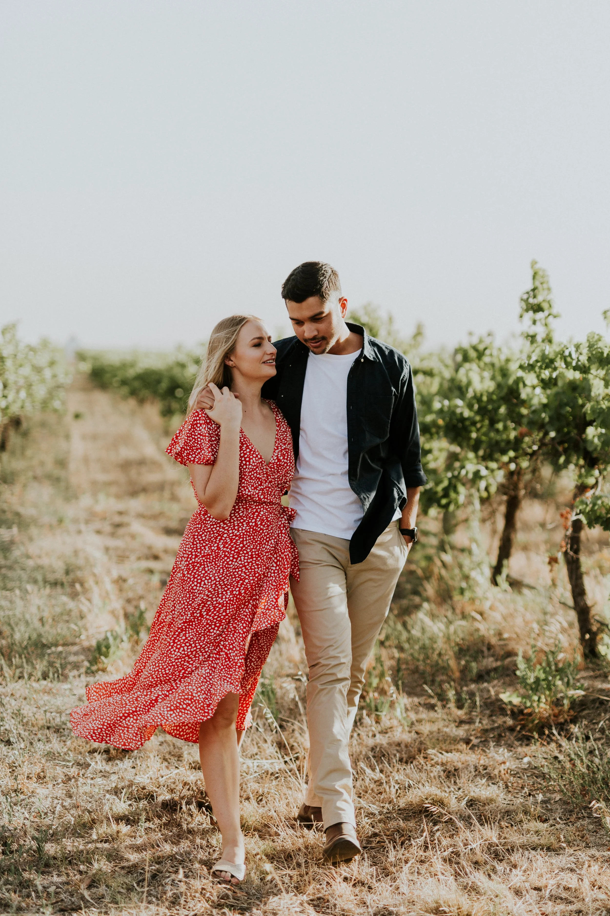 A young couple walking through a vineyard on a sunny day, smiling and enjoying each other's company.