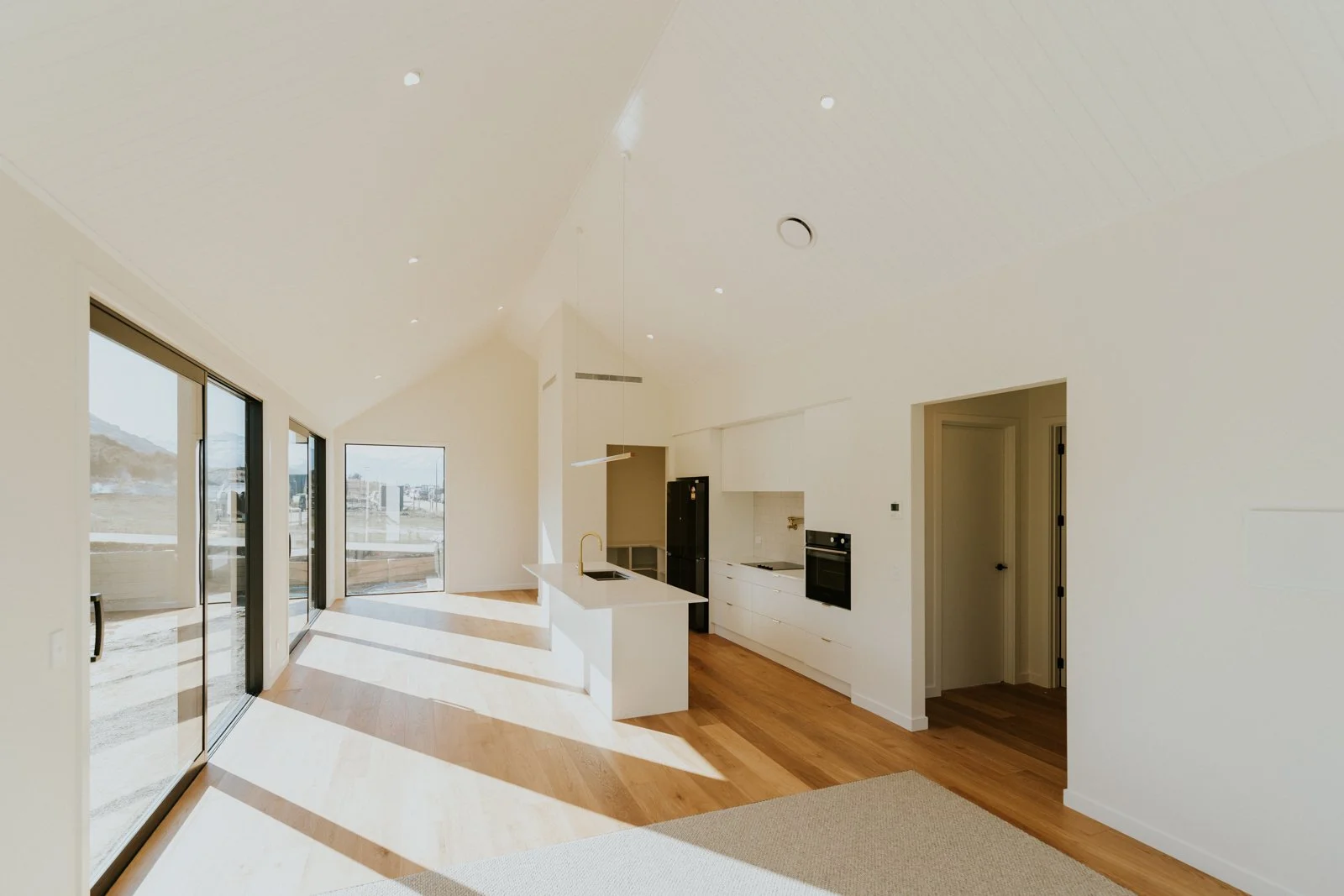 Modern minimalist kitchen with white cabinetry, a kitchen island with a gold faucet, and large glass sliding doors leading outside.
