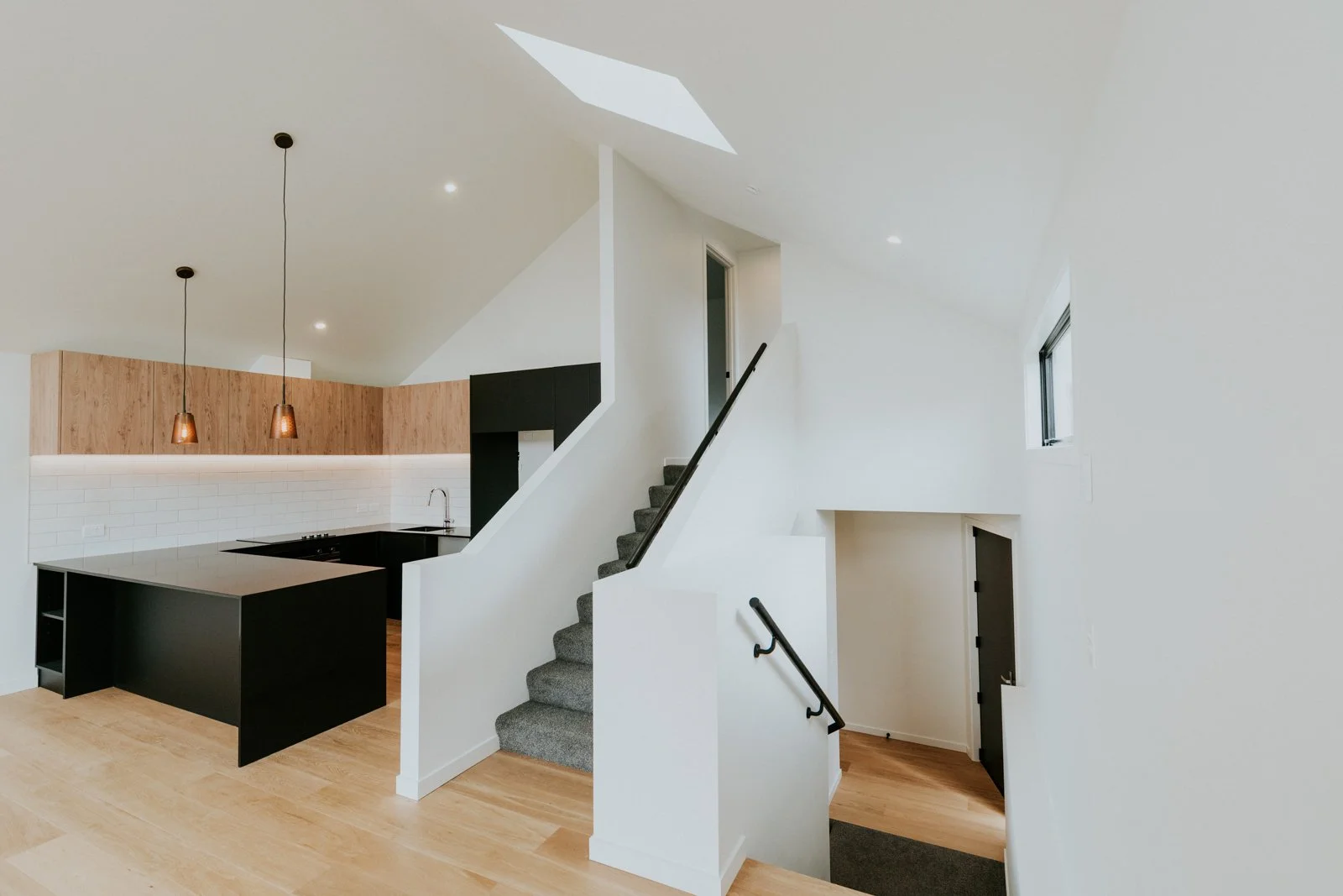 Modern interior with staircase, black kitchen counter, white walls, light wood floors, and minimalist design.