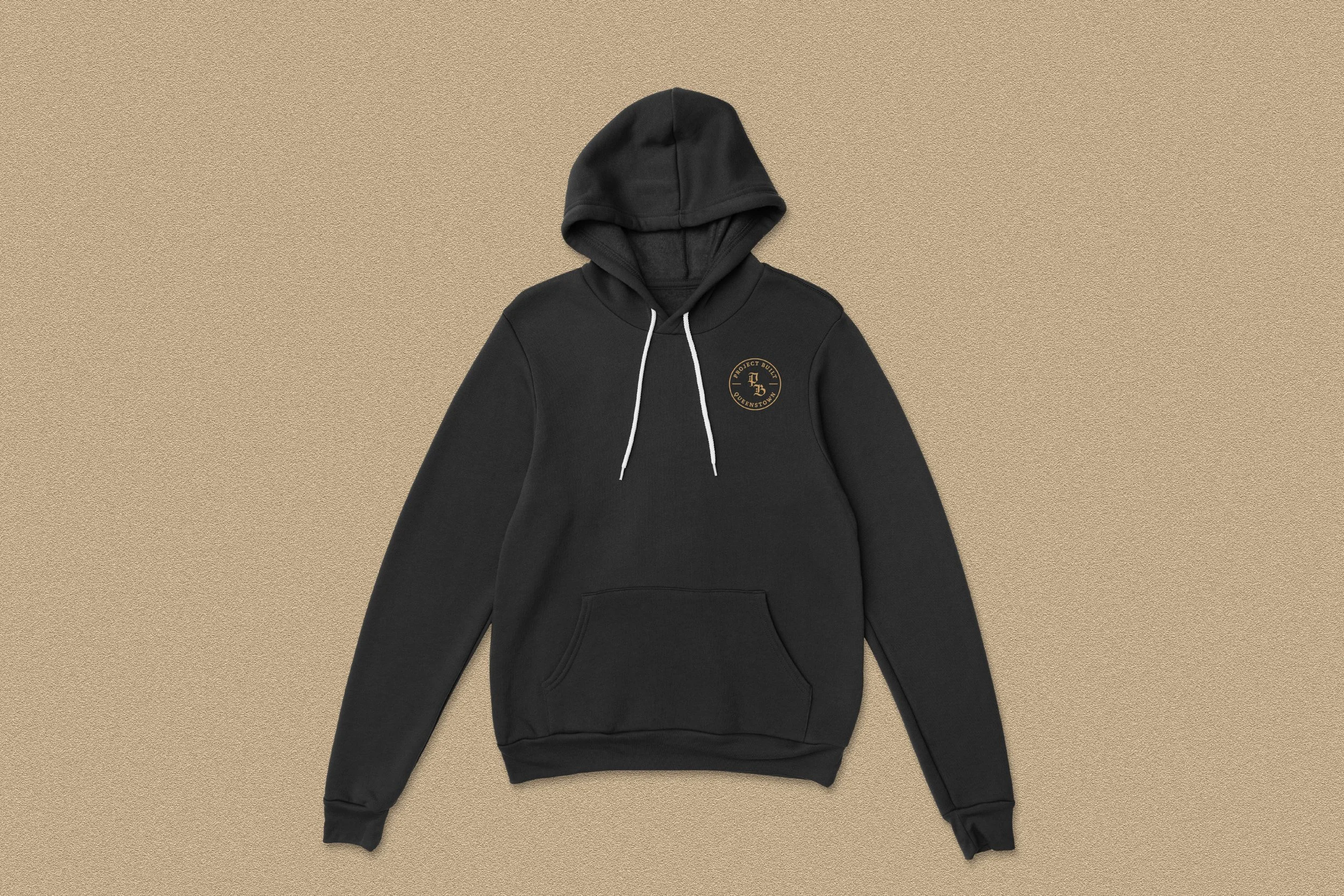 Black hoodie with a circular logo patch on the left chest area and white drawstrings, laid flat against a beige background.