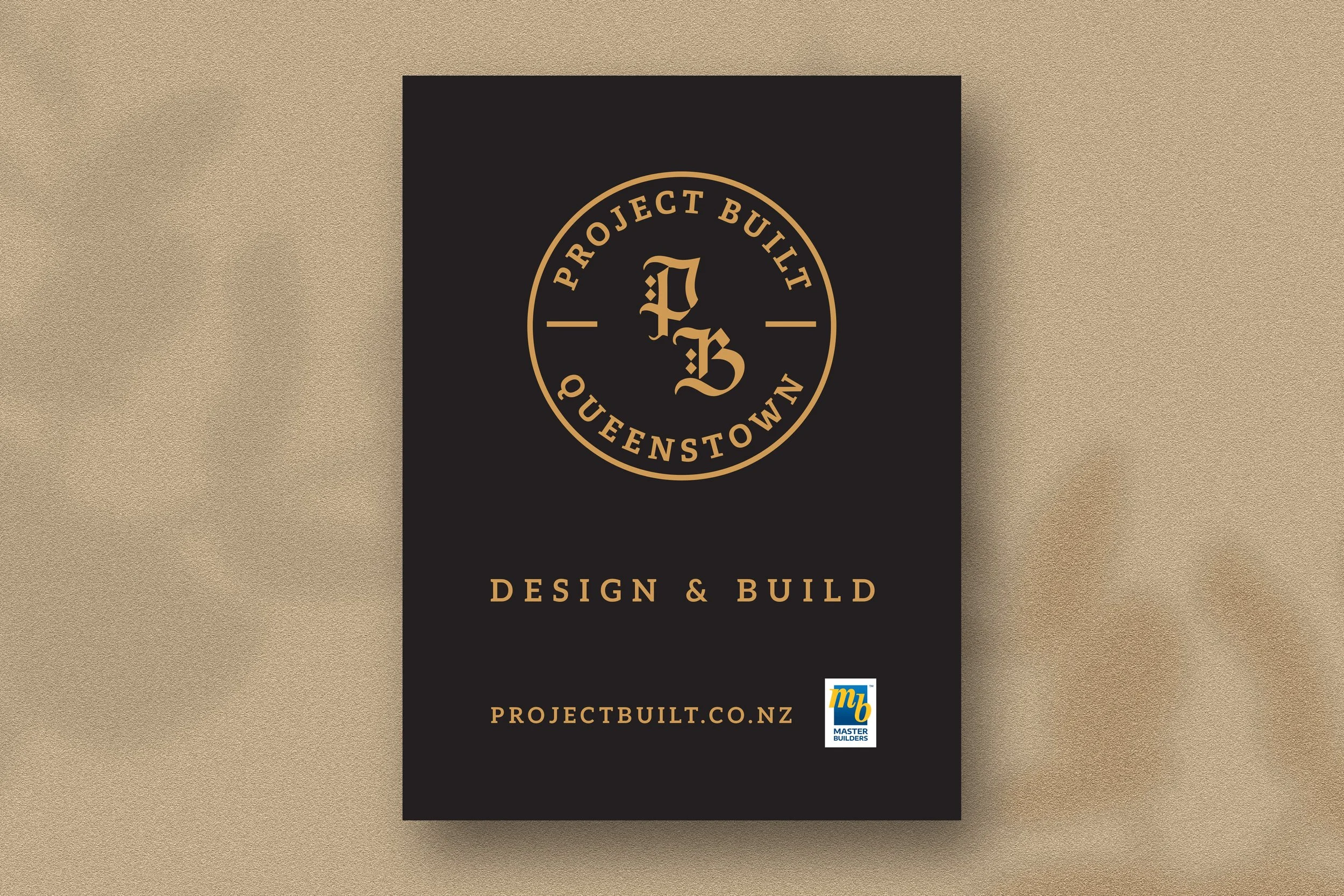 Black poster with gold lettering and logo for Project Built Queenstown, featuring a circular emblem with 'PB' in stylized font. Text reads 'Design & Build' and a website link 'projectbuilt.co.nz' at the bottom, alongside a small 'Master Builders' log