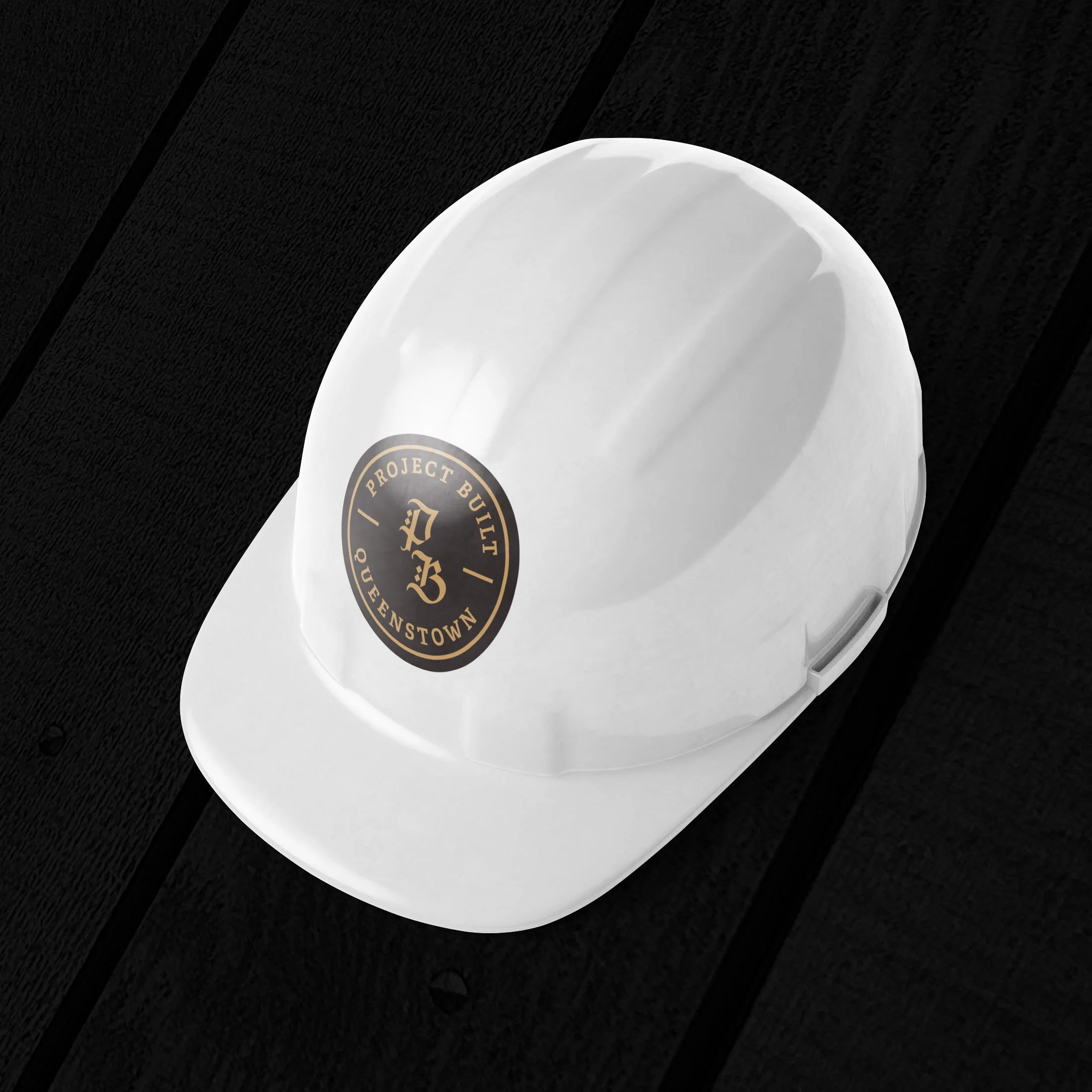 White construction hard hat with a black and gold sticker that reads "Project Built Queenstown."