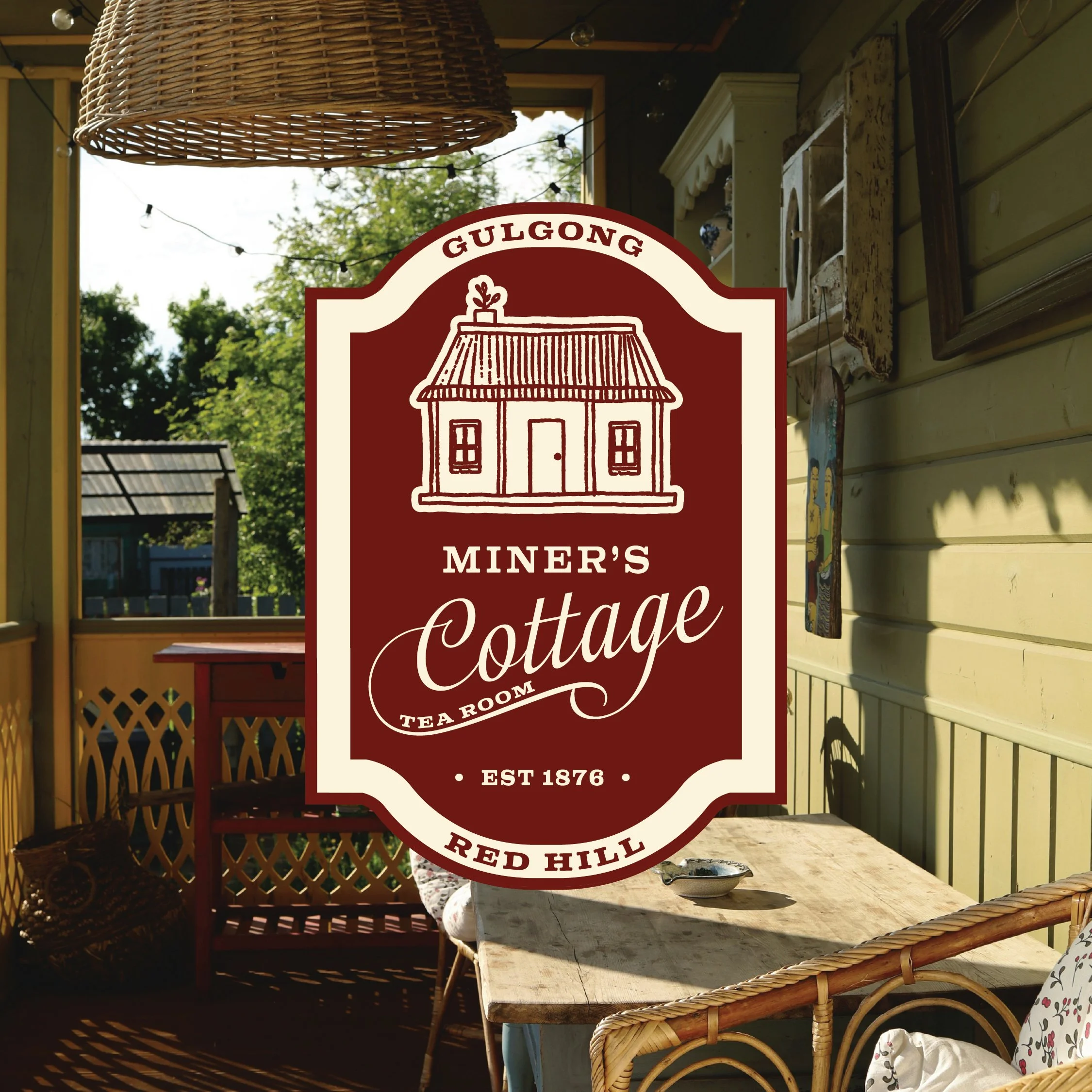 Sign for Miner's Cottage Tea Room at Red Hill, featuring a drawing of a cottage with a thatched roof, established in 1876, with a background of a cozy enclosed porch with wooden furniture and decorative items.