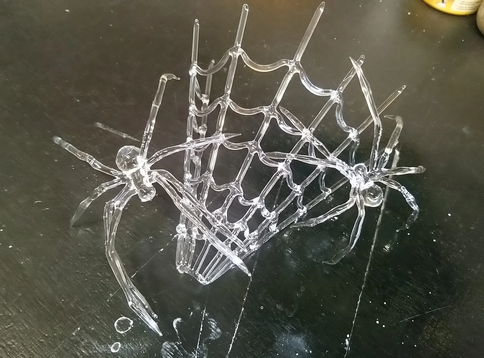 A glass spider web on a scratched black surface, with two glass spiders on each side
