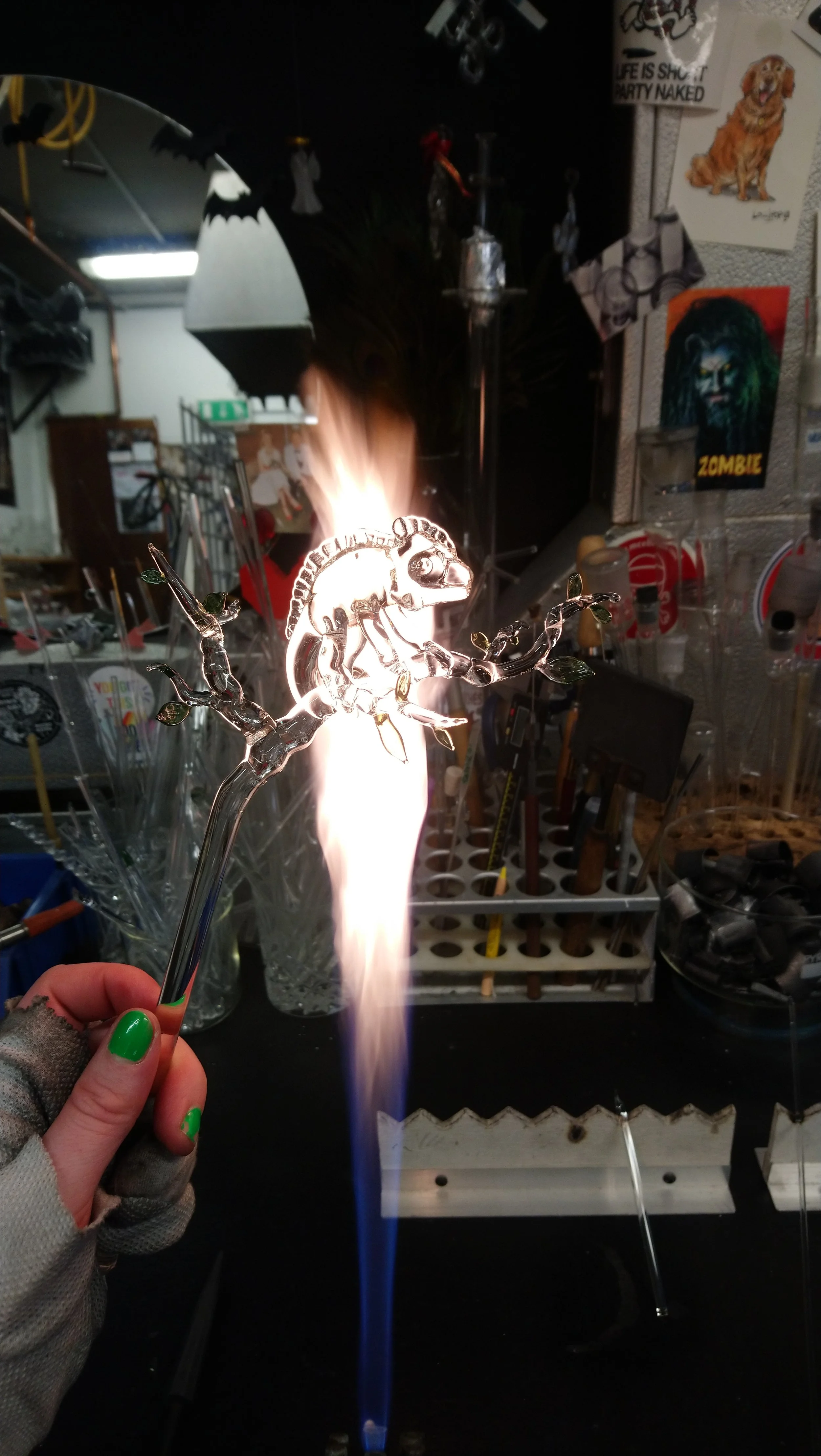 Glass chameleon on a glass stick being held in front of a flame in a workshop