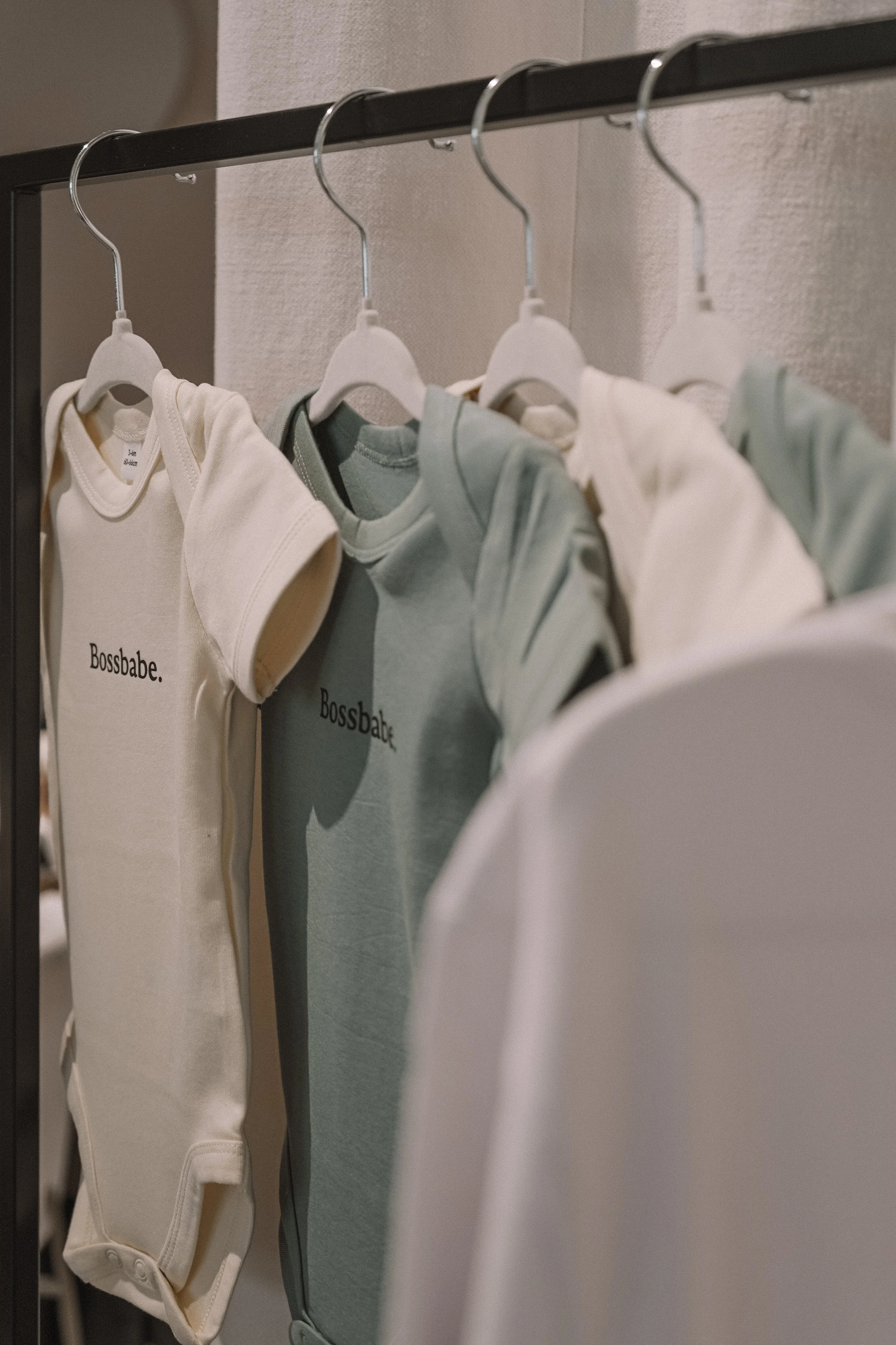 Baby clothes hanging on a rack, including onesies and shirts with the word 'Bossbabe' printed on them.