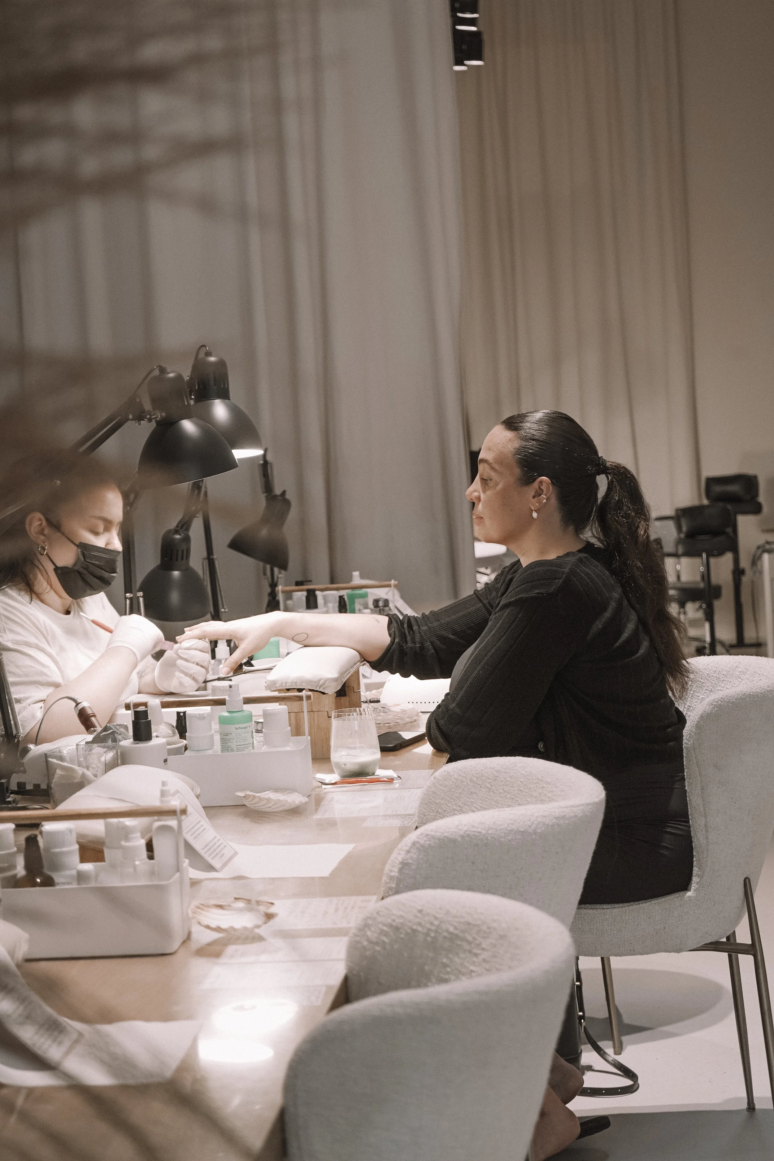 A woman receiving a manicure at a nail salon, with a technician wearing a face mask and gloves.