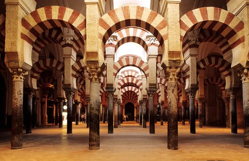 Interior view of the Mosque-Cathedral of Córdoba, featuring multiple red and white striped horseshoe arches supported by columns.