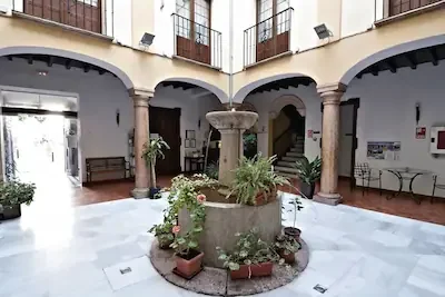 Indoor courtyard with a central fountain, potted plants, benches, and arches supported by stone columns.