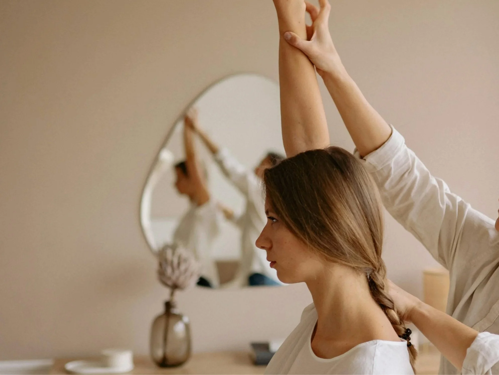 A woman stretching her arms above her head with the help of a physiotherapist.