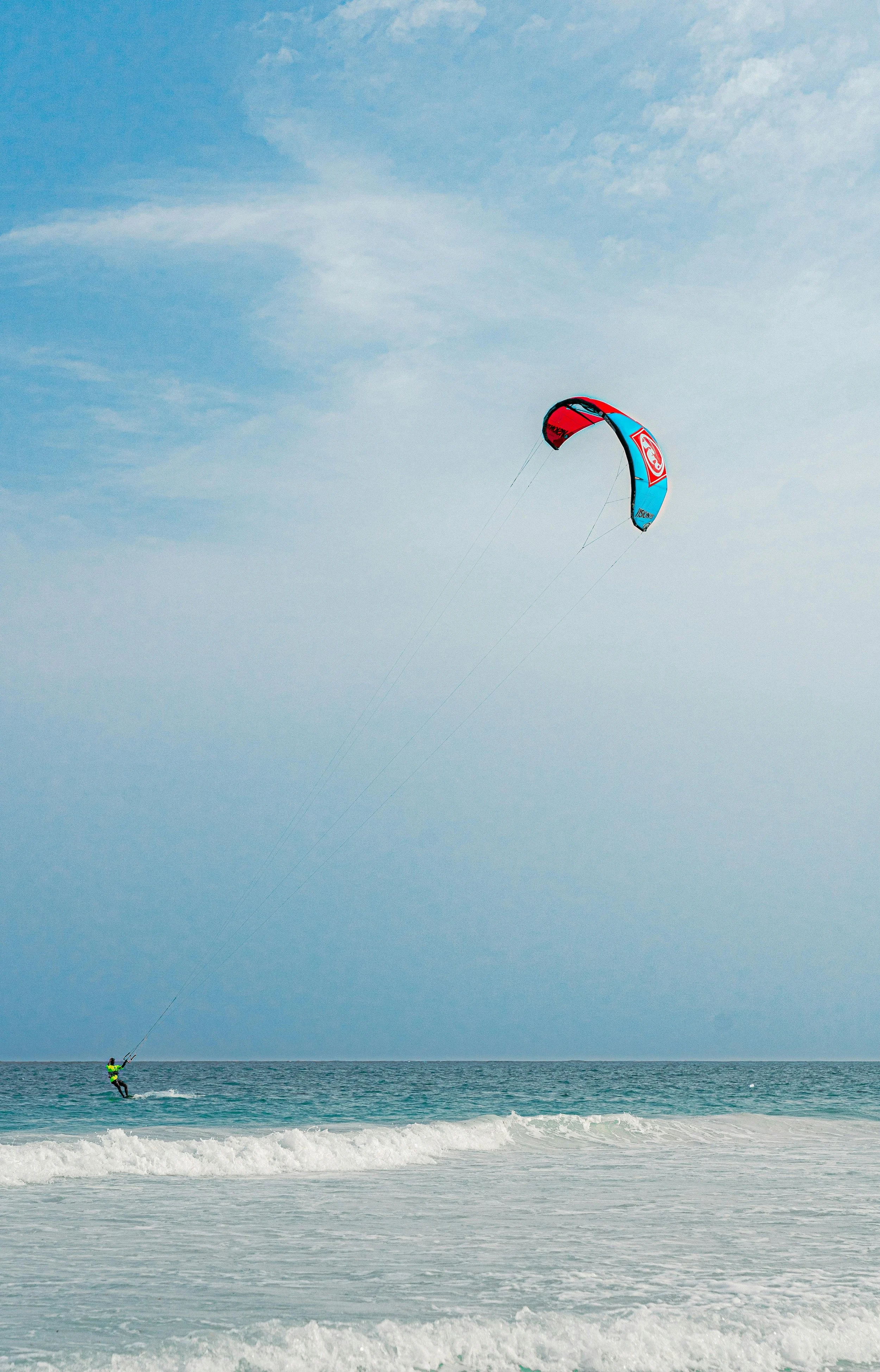 Person kiteboarding on the ocean, with a blue sky and a few clouds.