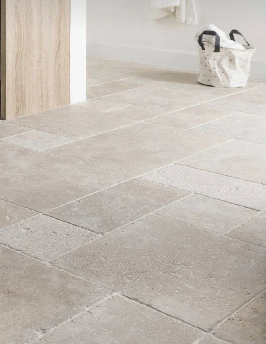 Close-up of beige tile flooring and a paper bag on the floor near the wall.