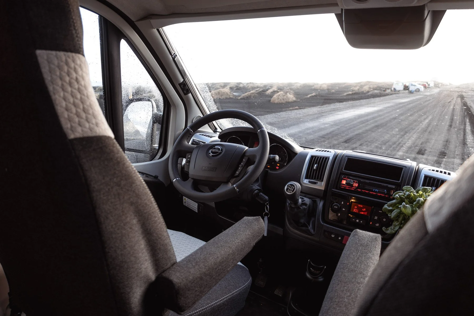 Innenansicht einer Campervan-Fahrerkabine mit Lenkrad, Schaltknüppel und Armlehne, Blick auf die winterliche Straße durch die Frontscheibe.