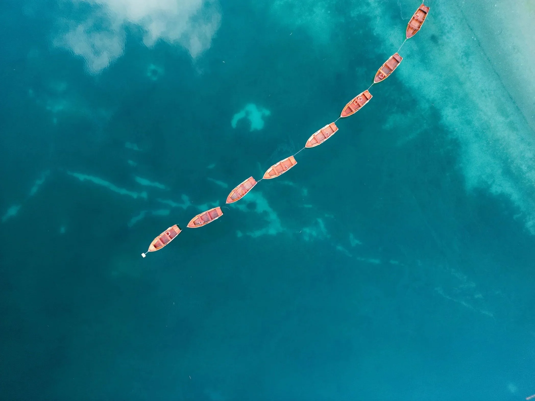 Luftaufnahme von sieben Booten in einem blauen See in den Dolomiten.