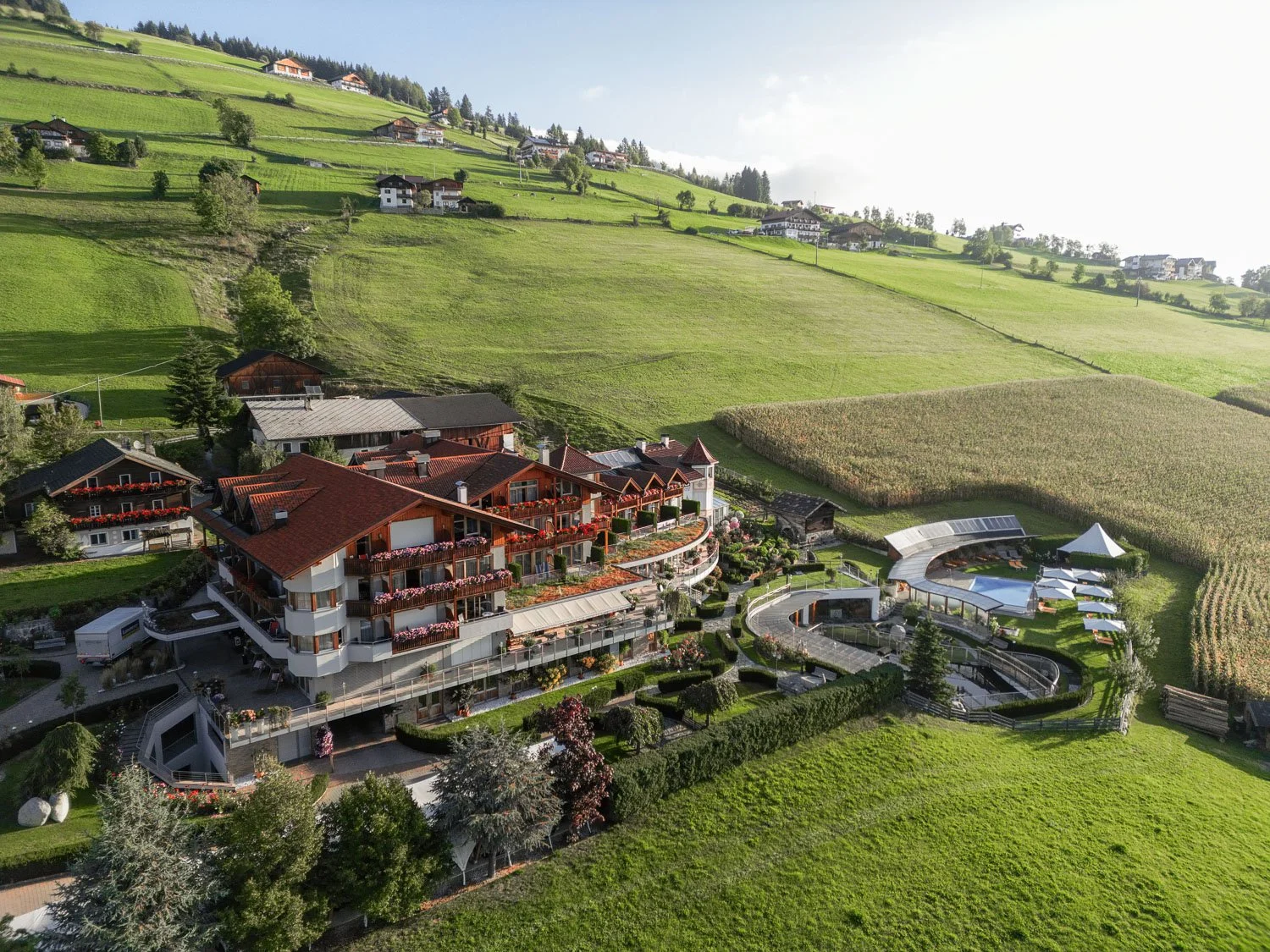 Luftaufnahme eines modernen Hotels mit Pool im Garten, umgeben von grünen Feldern und Hügeln in einer ländlichen Gegend.