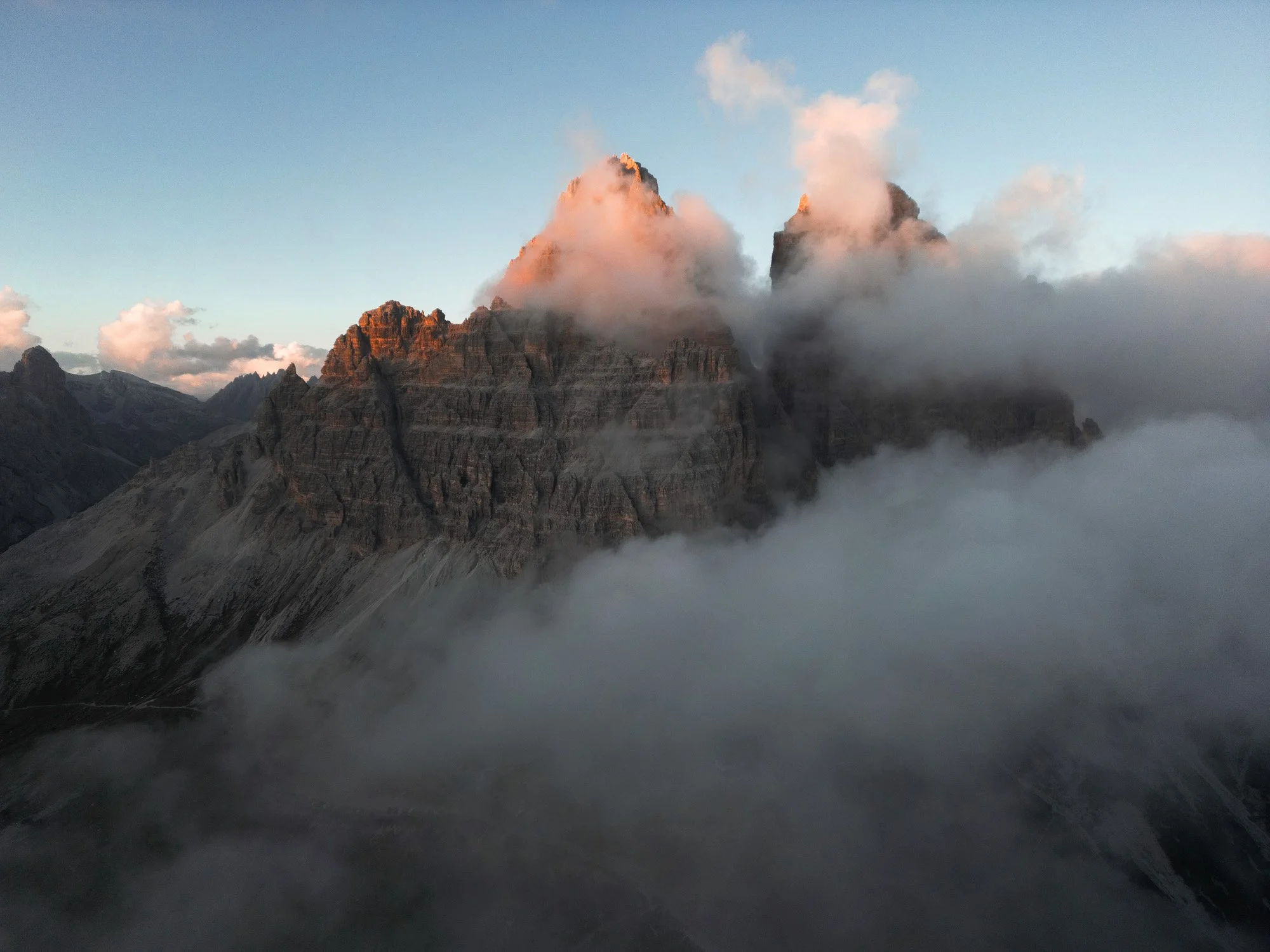 Berggipfel in Wolken eingehüllt bei Sonnenuntergang, mit Nebel im Tal.