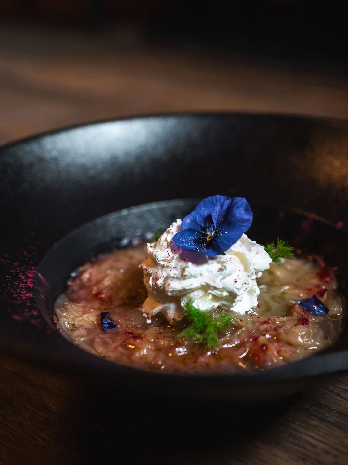 Ein Gericht in einer schwarzen Schale mit Sahne, Kräutern und blauen Blüten.