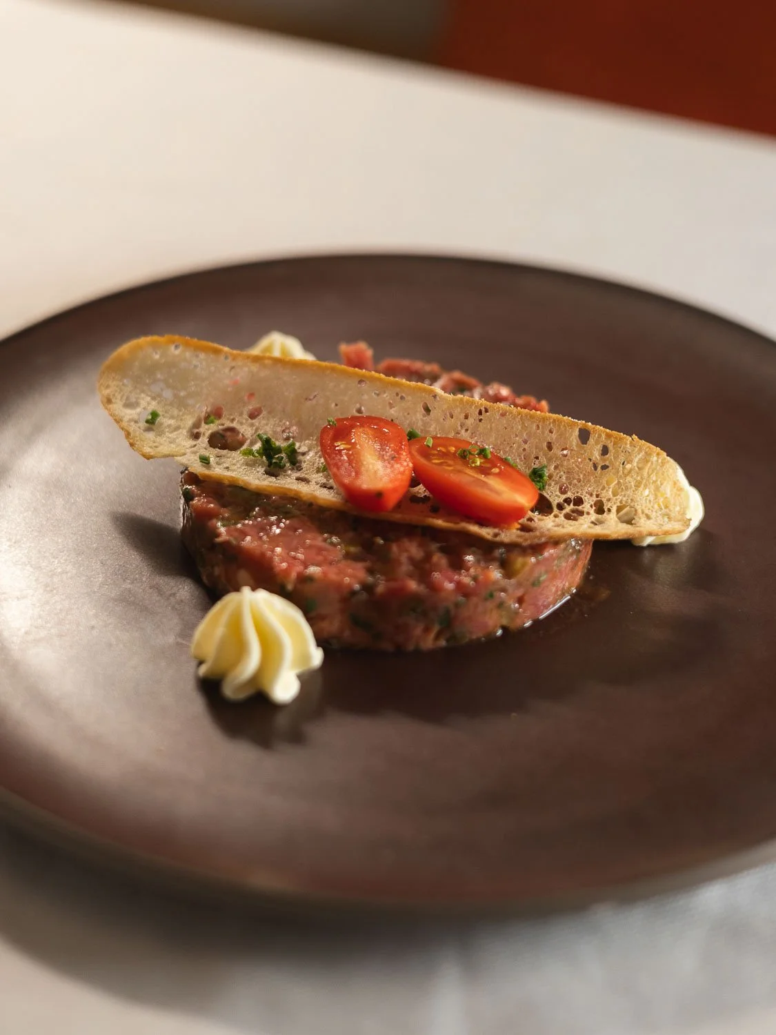 Feines Gericht mit rohem Rindfleisch-Tatar, einer knusprigen Scheibe Brot mit Tomatenscheiben, eine kleine Pestospur, und einer kleinen Portion Maiscreme.