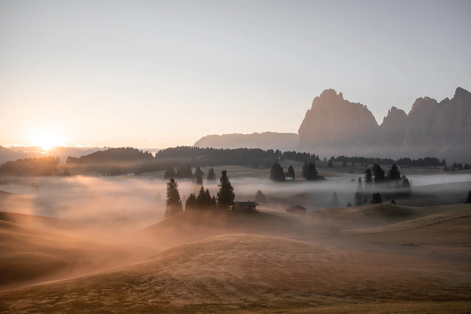 Morgenlandschaft mit Nebel in Tälern, Hügeln und Bergen im Hintergrund, Sonnenaufgang am Horizont.