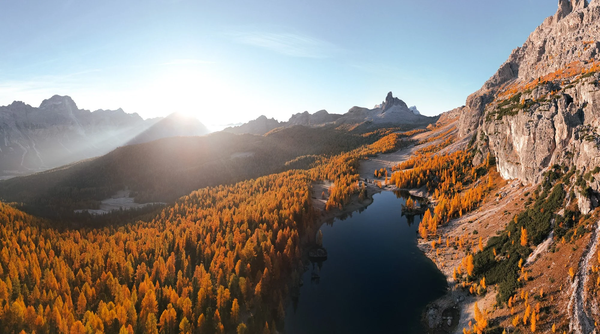 Bergsee im Tal mit orange gefärbten Bäumen umgeben von Bergen bei Sonnenaufgang
