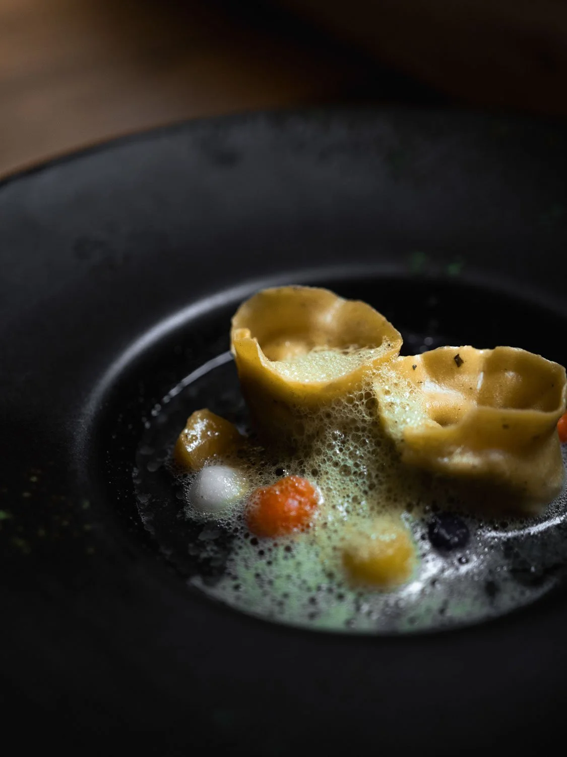 Ravioli in einem schwarzen teller, mit Eierschaum und kleinen Karotten.