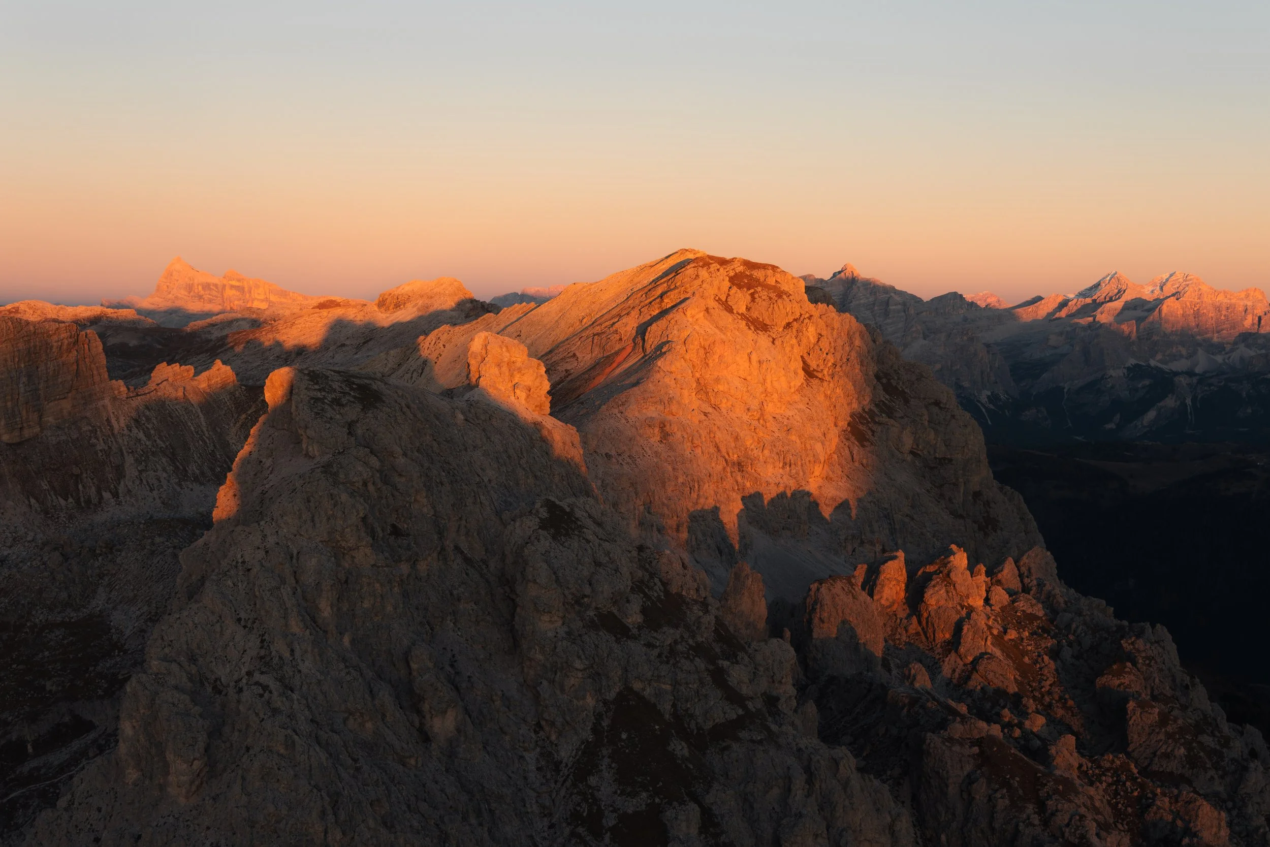 Berggipfel der Dolomiten bei Sonnenuntergang mit orange Beleuchtung, felsige Landschaft, klare Himmel.