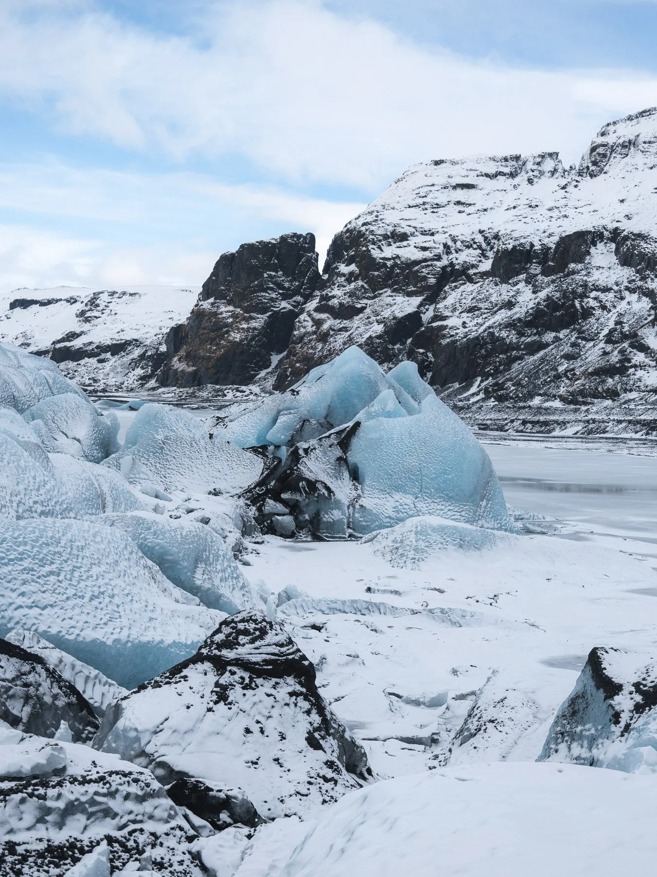 Gletschereis in einer verschneiten Berglandschaft mit Felsen und Himmel.