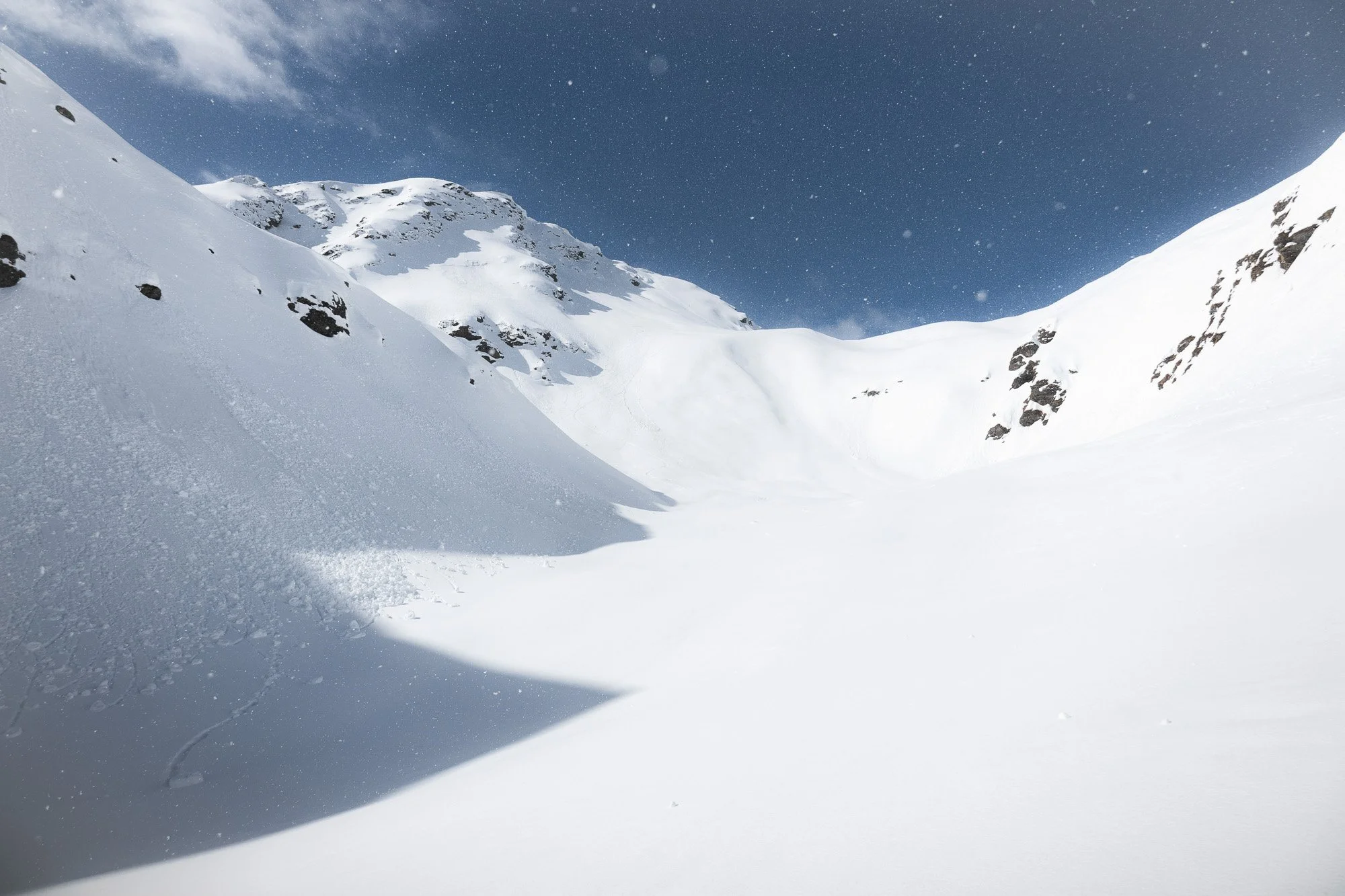 Schneebedeckte Berge unter bewölktem Himmel mit Schneefall in einer hohen Bergregion.