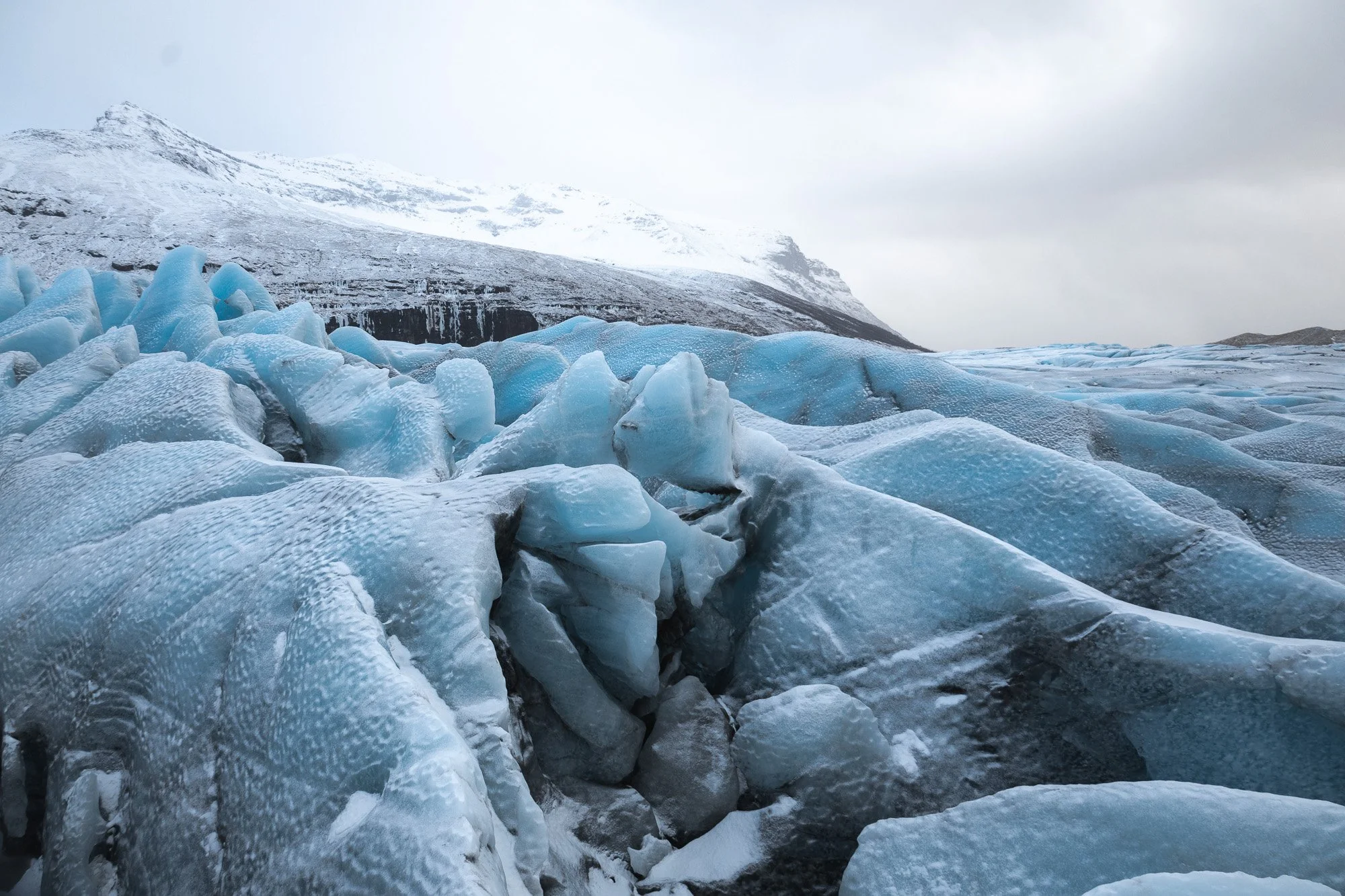 Blick auf vereiste Gletscher mit schneebedecktem Berg im Hintergrund in einer arktischen Landschaft.