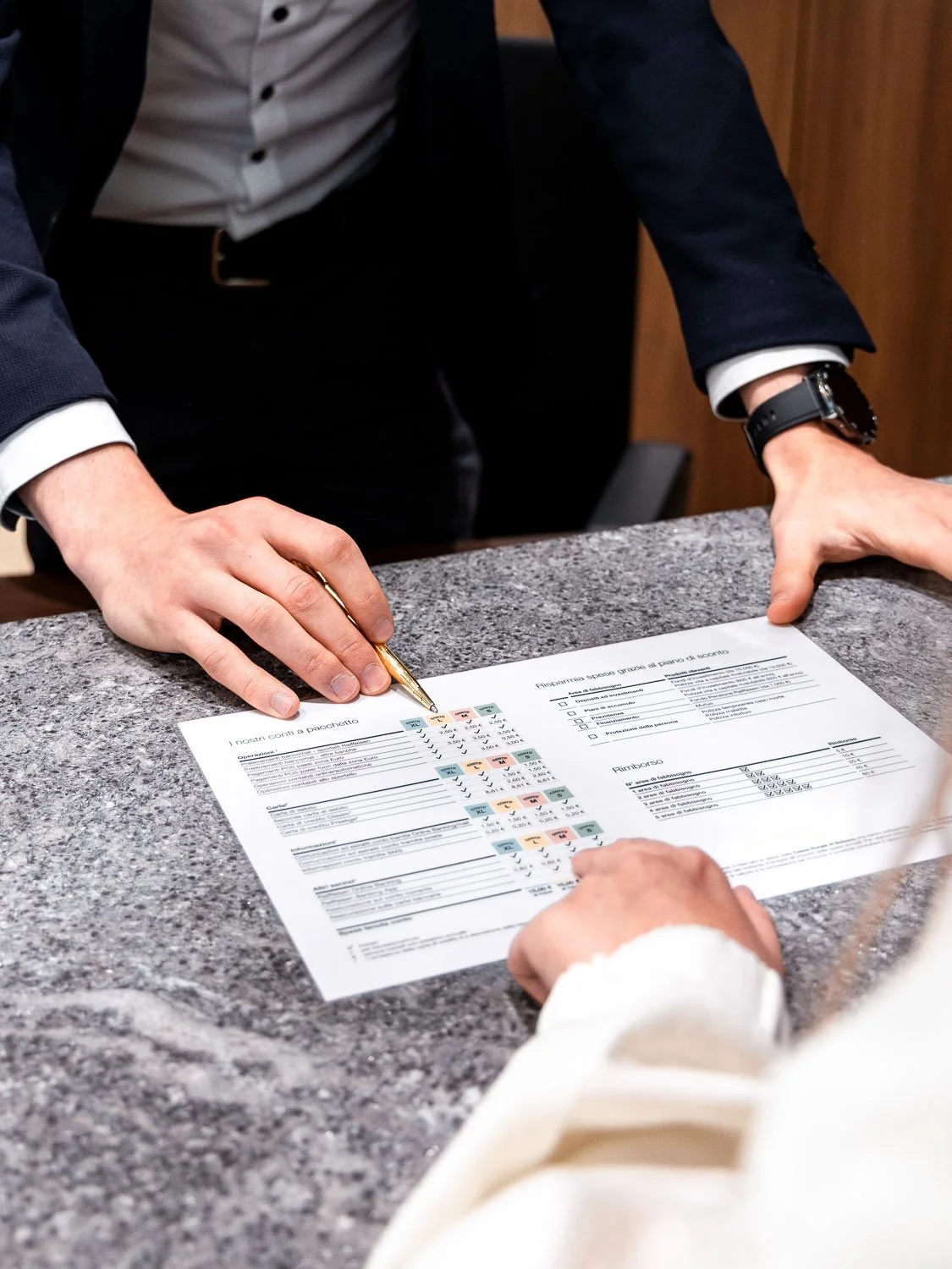 Geschäftsmann in Anzug mit Uhr beim Unterschreiben eines Dokuments auf der Empfangstheke.