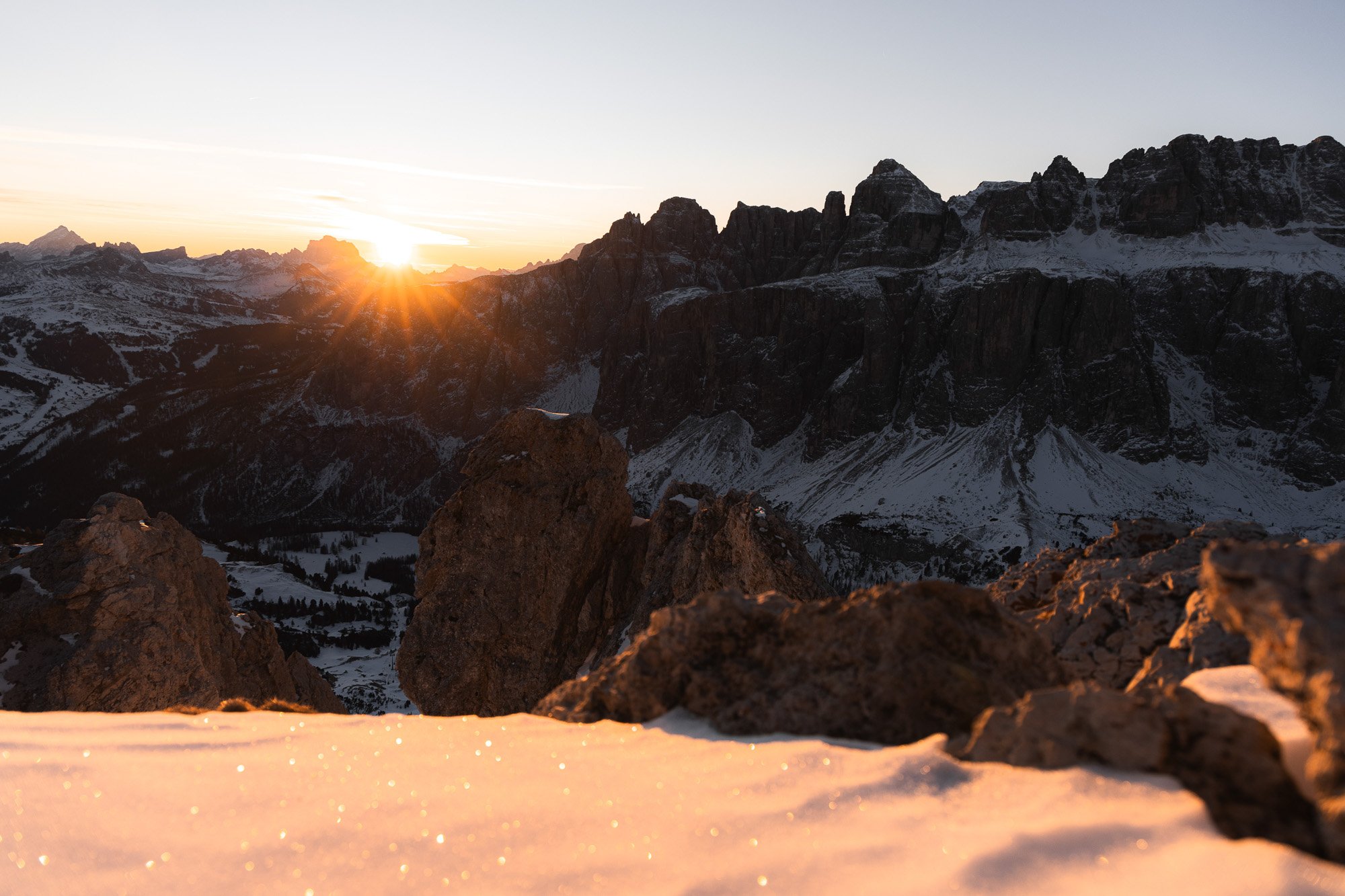 Berglandschaft bei Sonnenaufgang mit schneebedeckten Felsen und Bergen im Hintergrund.