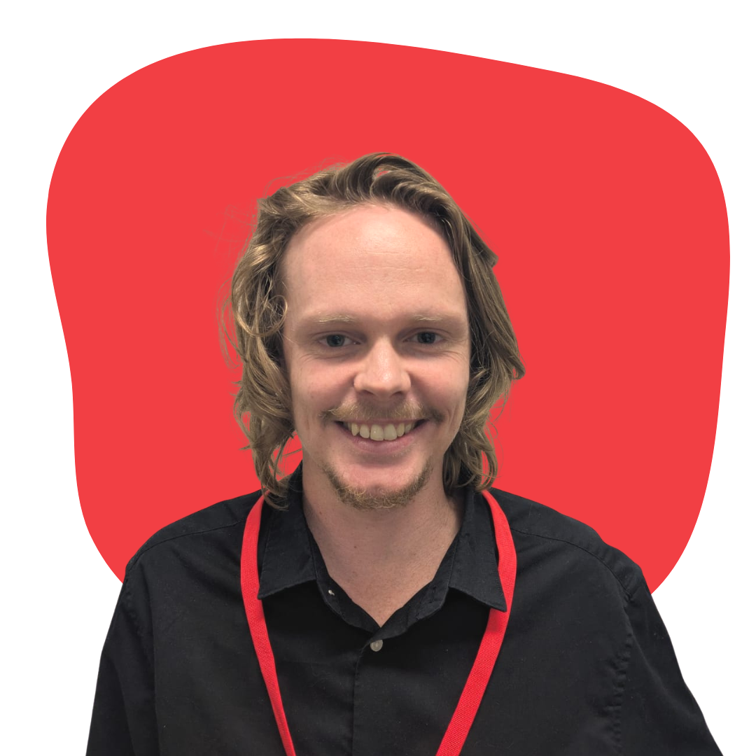 A smiling young man with shoulder-length wavy blond hair, wearing a black shirt and a red lanyard, against a red apple-shaped background.