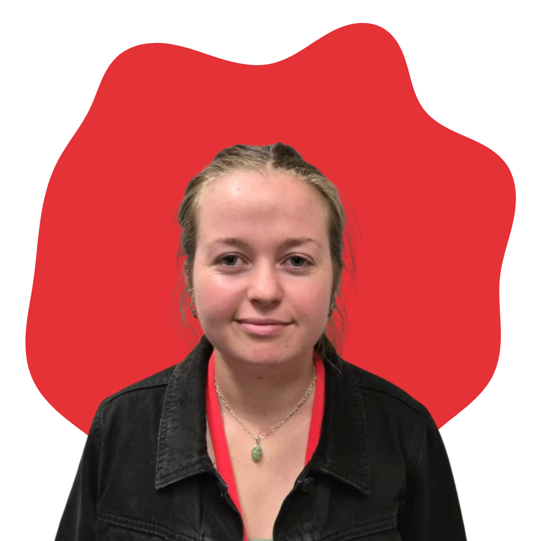 A young woman with blonde hair, wearing a black jacket and a necklace with a green pendant, standing in front of a red abstract shape on a white background.