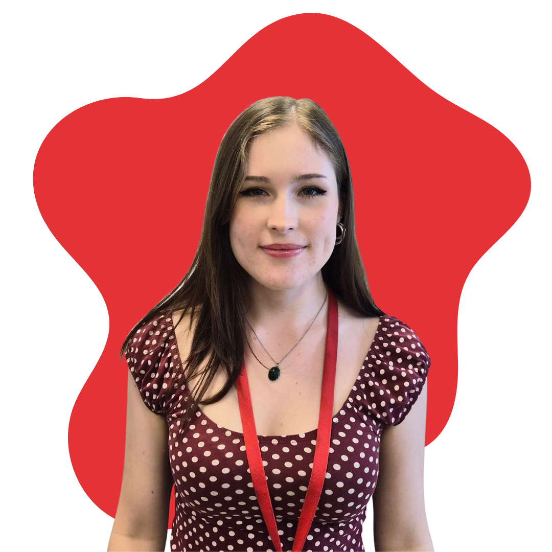 A young woman with long brown hair, wearing a maroon polka dot dress, a necklace with a black pendant, and a red lanyard, standing in front of a red abstract background.