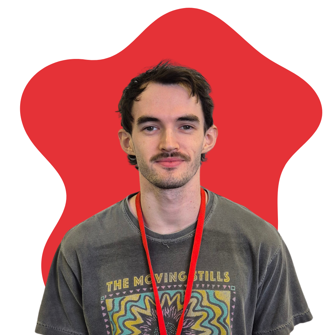 A young man with dark hair and a mustache, wearing a graphic t-shirt and a red lanyard, standing in front of an abstract red shape.