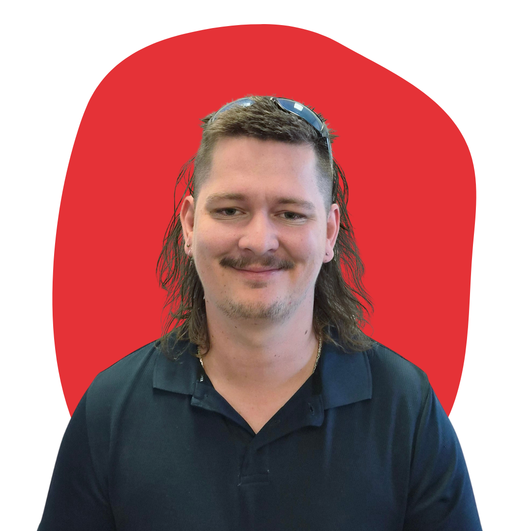 A man with shoulder-length brown hair, wearing sunglasses on his head, earrings, a black collared shirt, and a thin mustache and beard, smiling in front of a red abstract background.