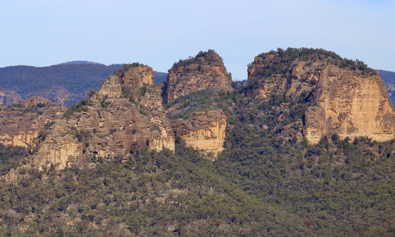 Rock formations with steep cliffs and sparse vegetation in a mountainous landscape under a clear sky.