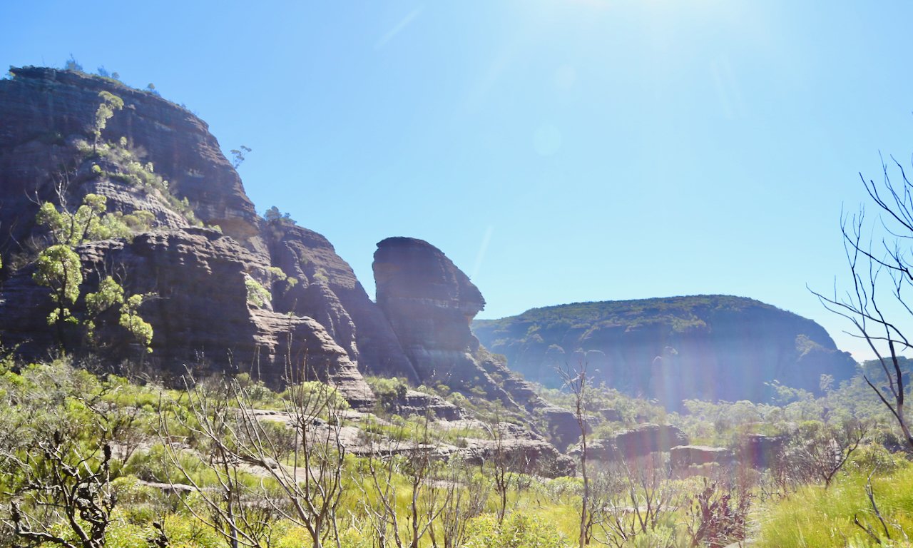 Sunny day in a rocky, mountainous landscape with sparse vegetation and a clear blue sky.
