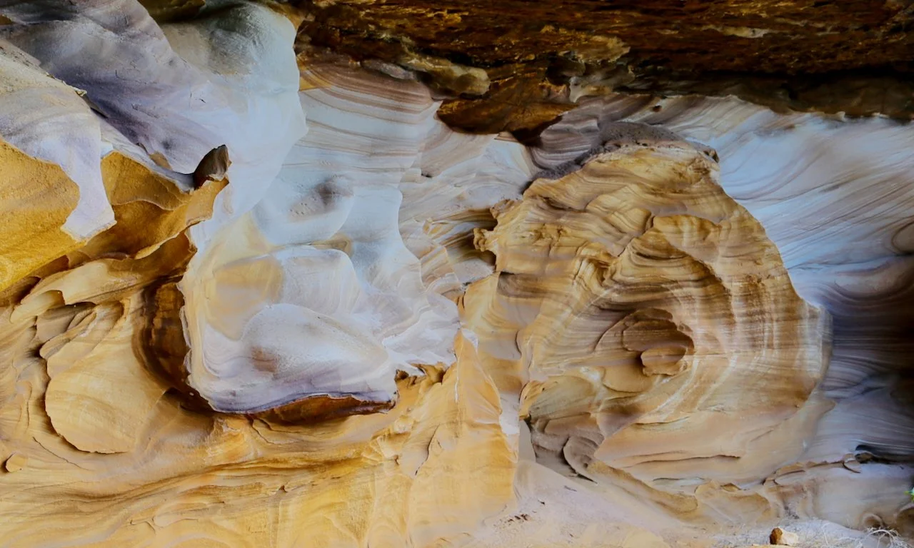 Colorful layered rock formations inside a slot canyon with smooth, flowing shapes and striations in shades of white, yellow, brown, and purple.