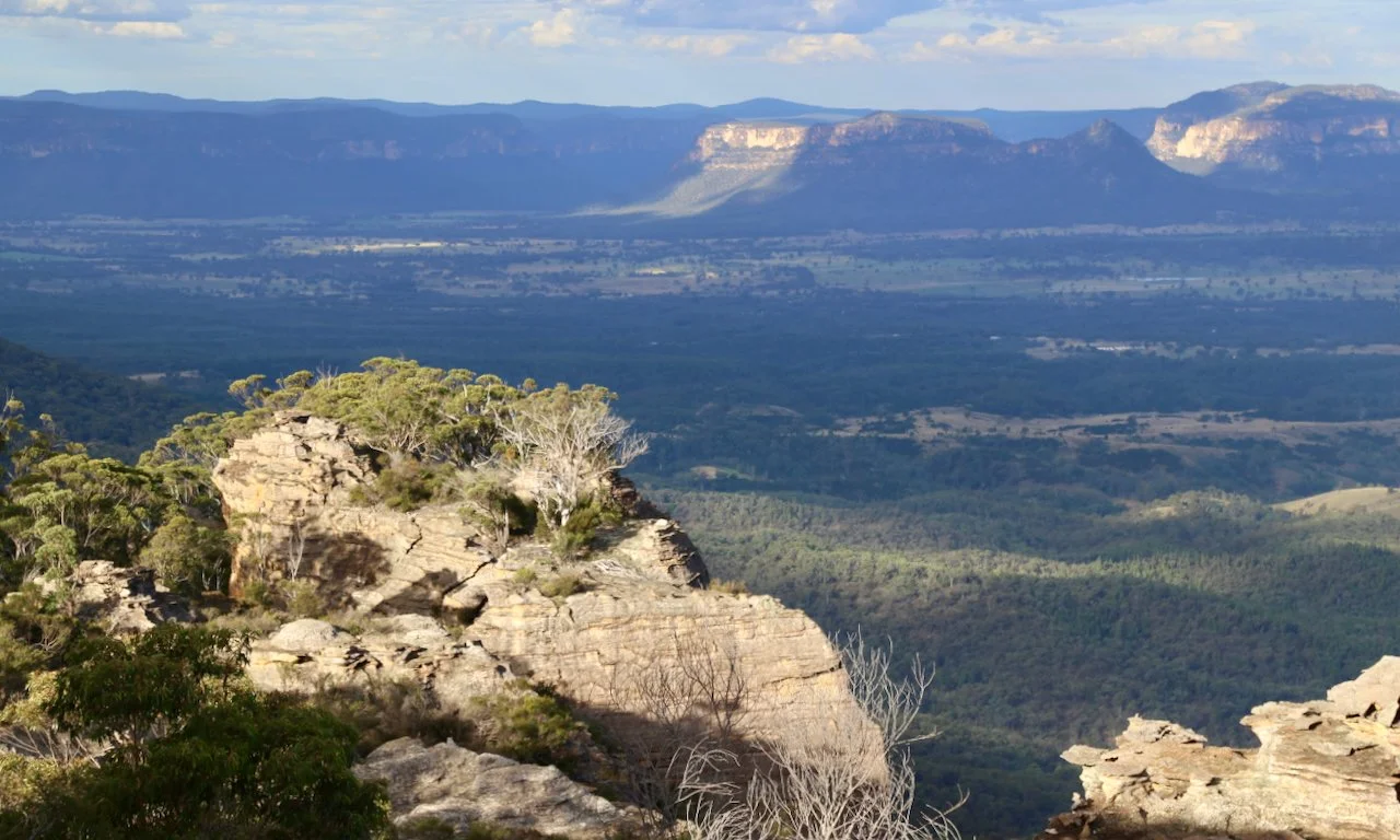 Scenic view of rocky cliffs and trees with mountains in the background under a partly cloudy sky.