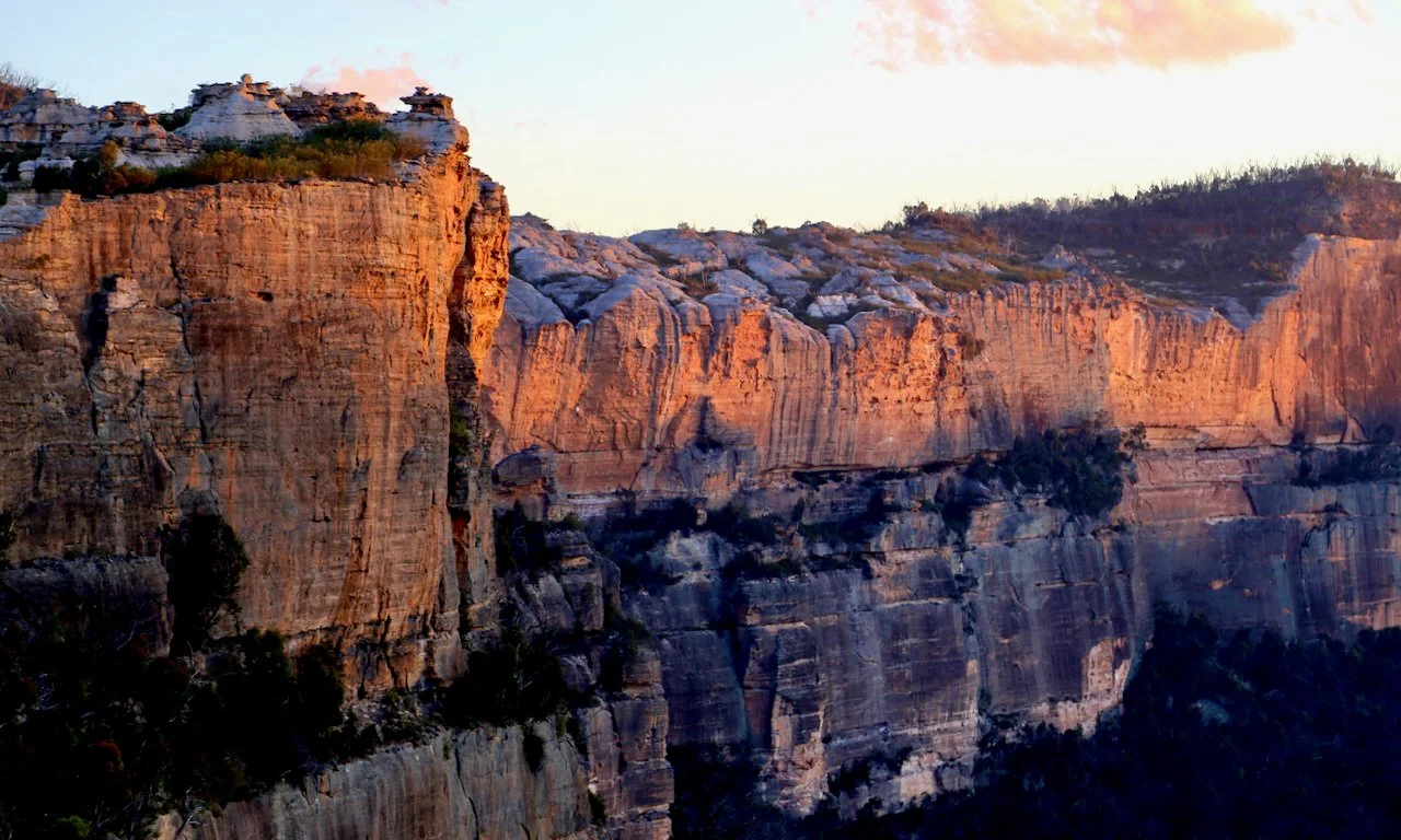 Sunset over rocky canyon cliffs with sparse vegetation