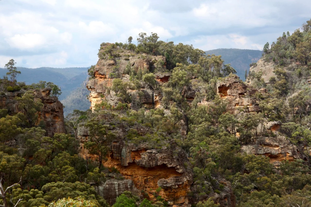 Steep rocky mountain landscape with dense green forest on cliffs and blue cloudy sky in the background.