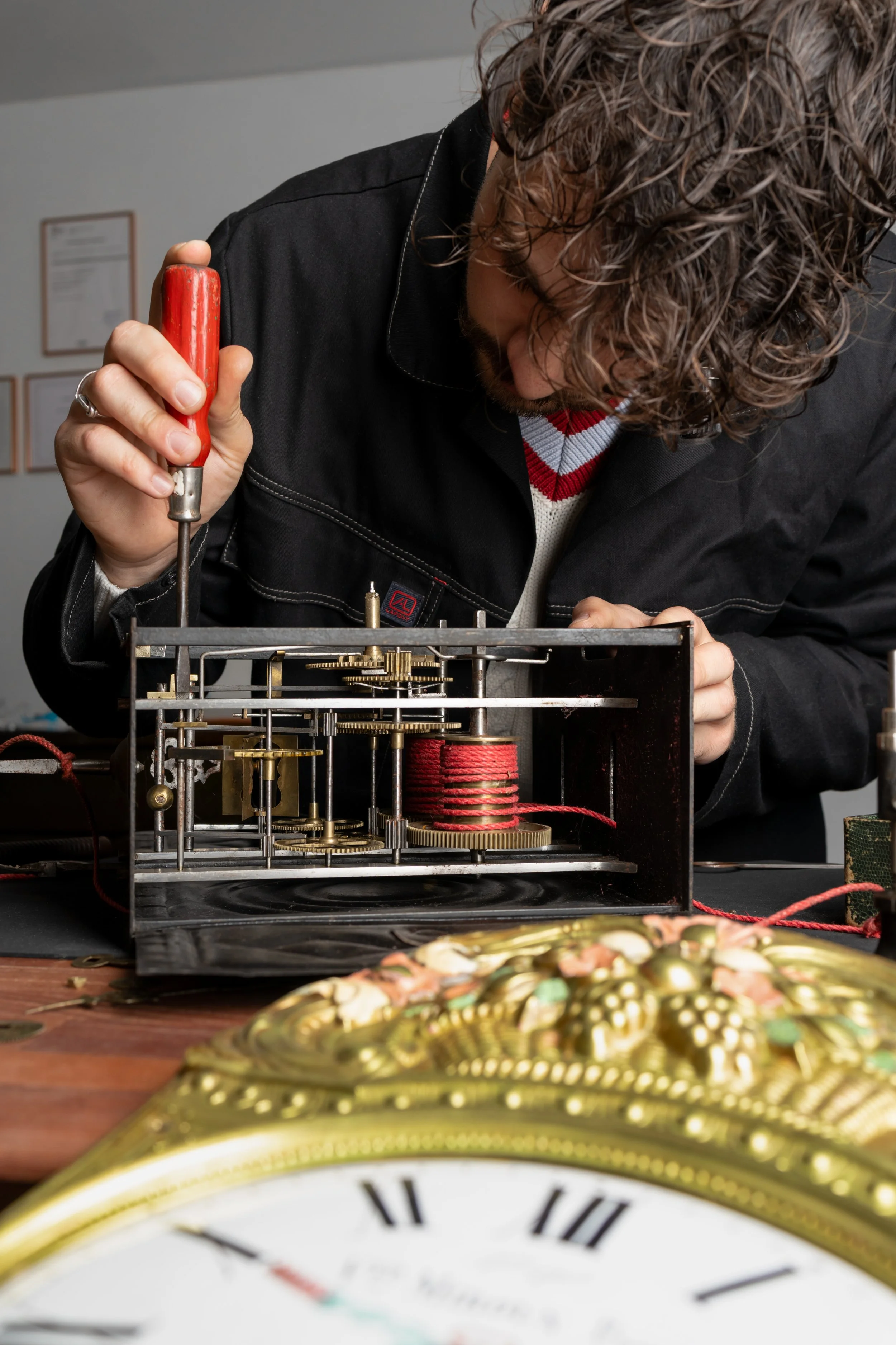 Un homme répare un mécanisme d'horloge en utilisant un tournevis dans un atelier.