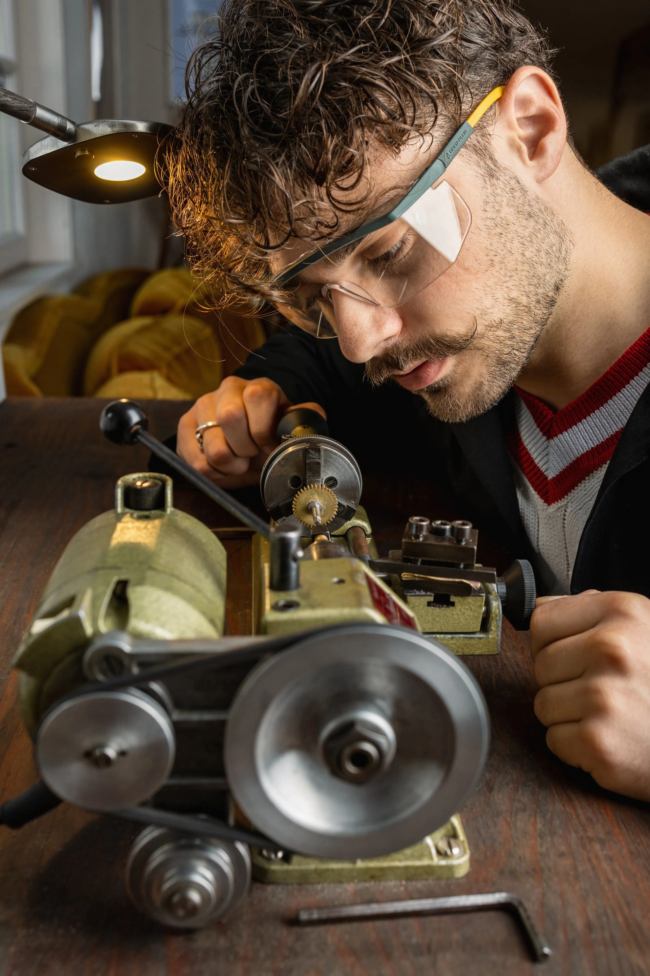 Jeune homme regardant attentivement une machine en utilisant une loupe de précision, portant des lunettes de sécurité, en intérieur.