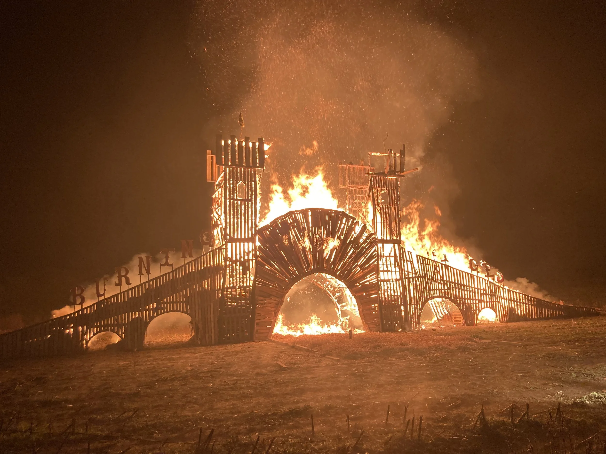 A structure on fire with tall flames and smoke, resembling a burning amusement park ride or large sculpture, at night.
