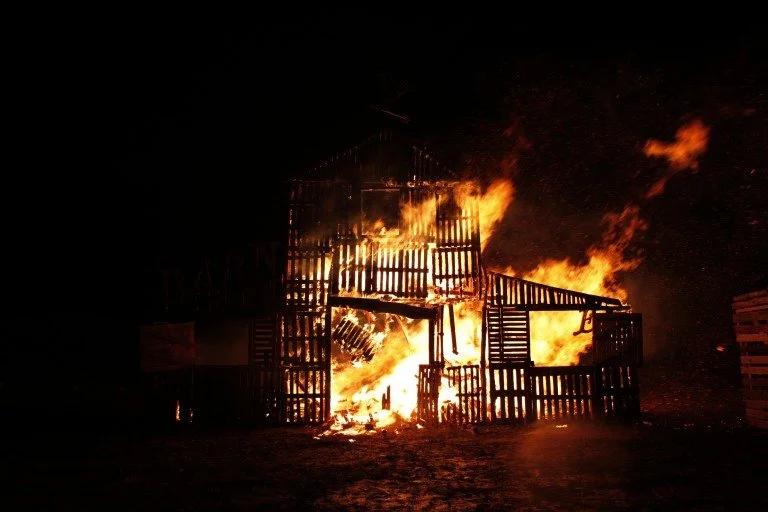 A large wooden structure is on fire with flames and smoke rising into the night sky.